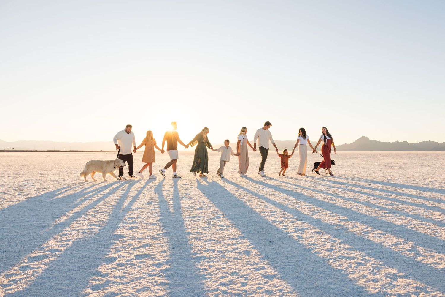 A group of people holding hands while walking in a line across a bright white salt flat terrain.
