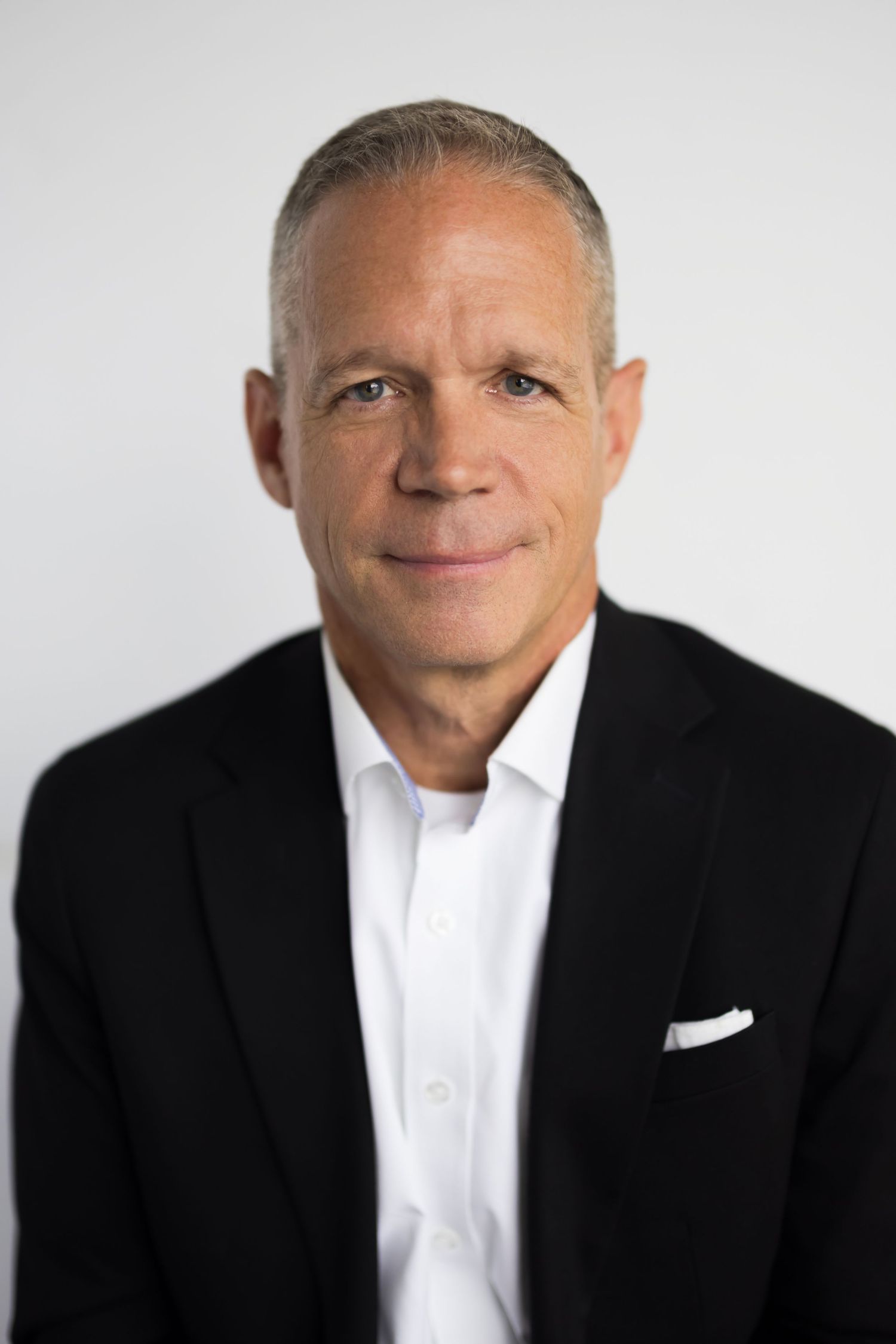 Professional headshot of a person in a black suit and white shirt against a light background.