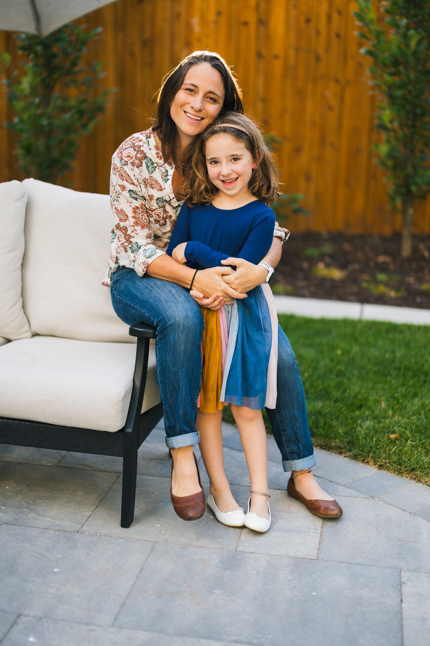 Parent and child sitting together on outdoor furniture in backyard setting.