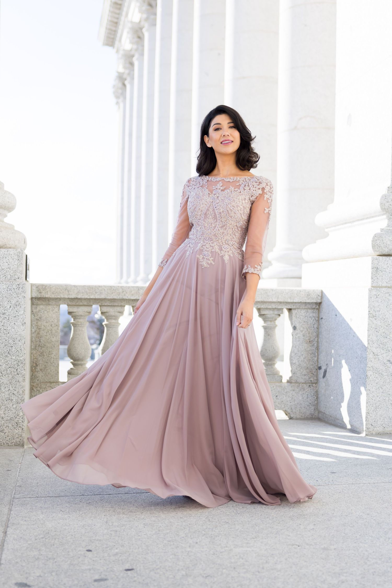 Elegant mauve chiffon gown with lace bodice and flowing skirt photographed against white classical columns.