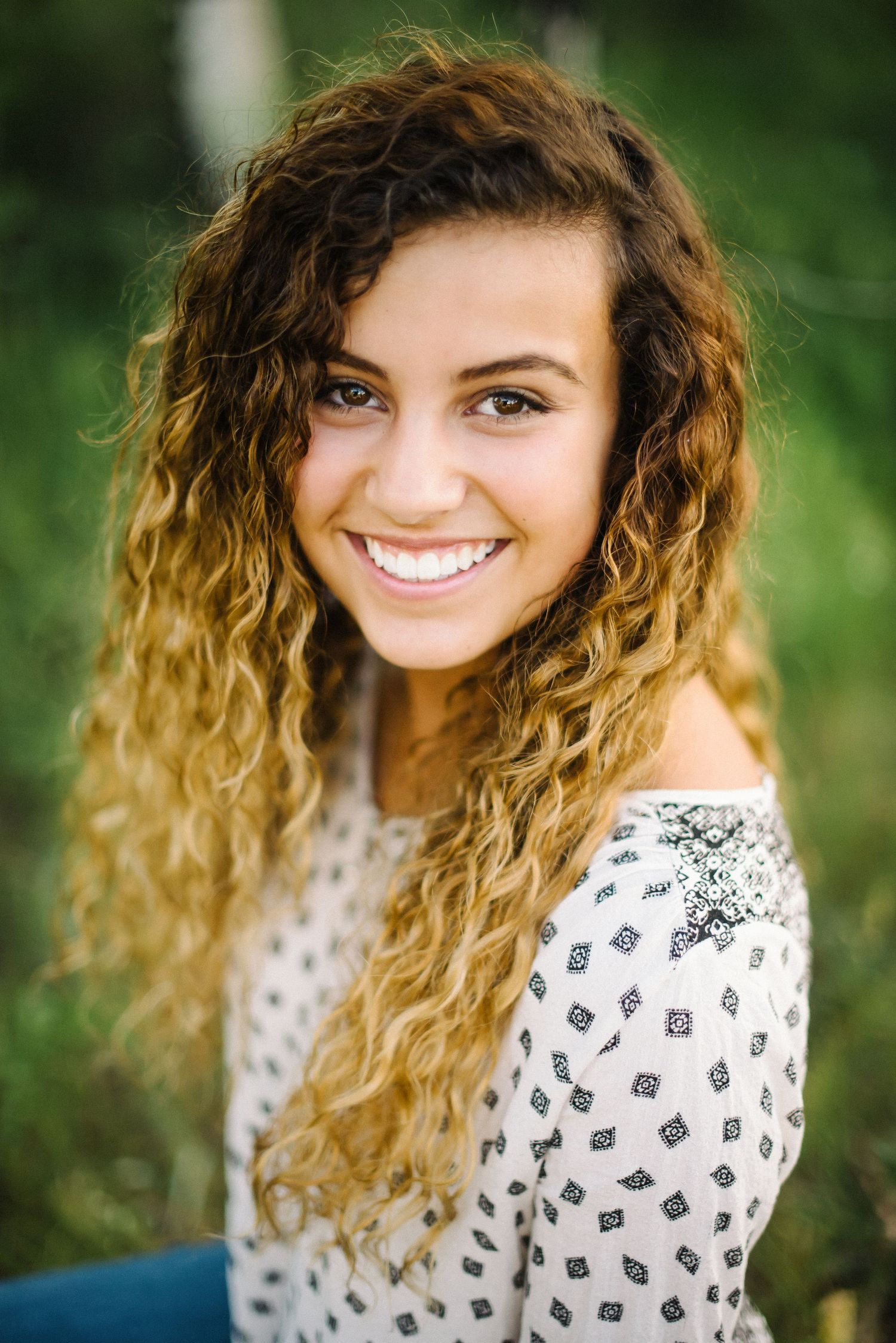 Portrait of person with long curly ombre hair wearing floral top outdoors.