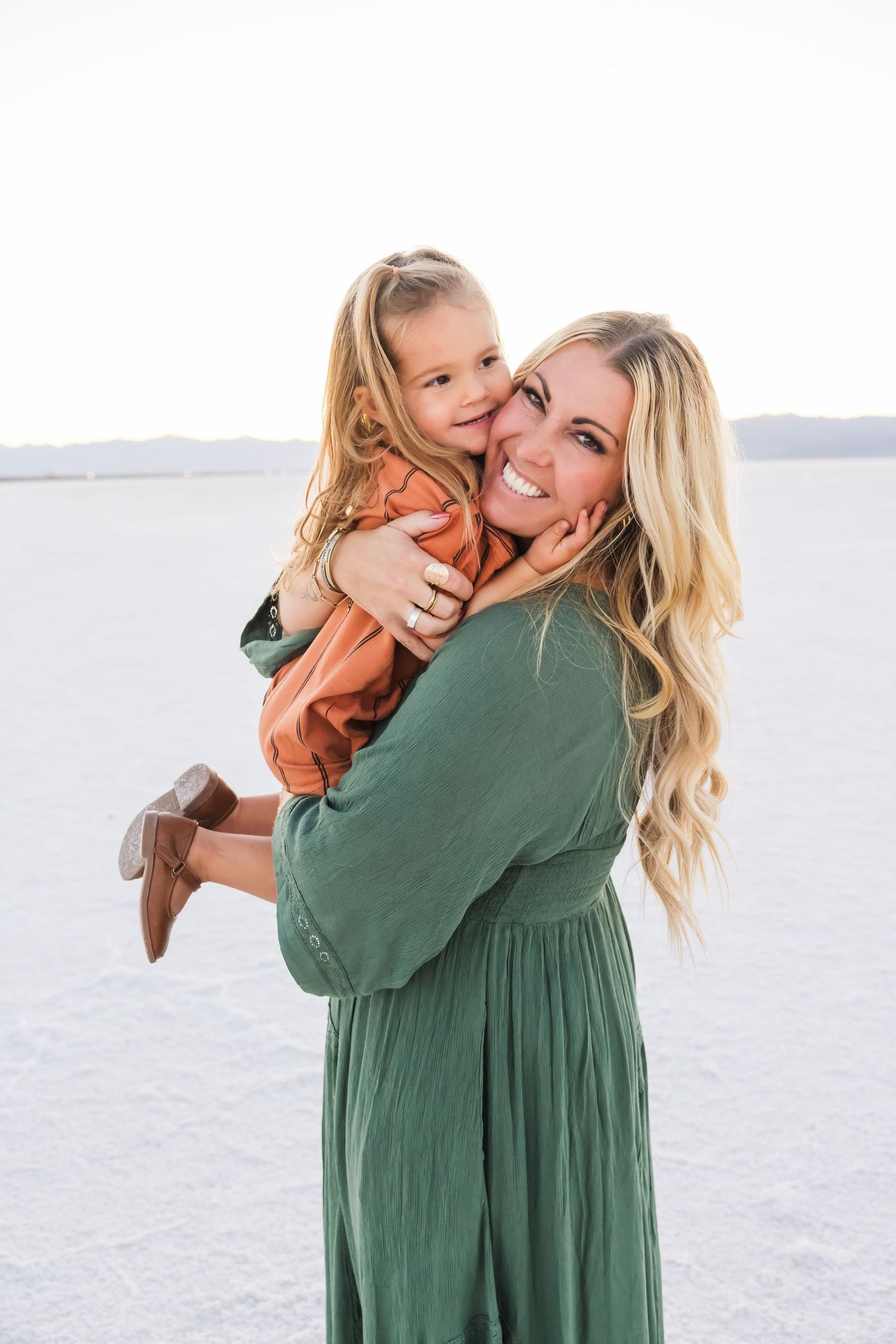 A tender moment between parent and child wearing green and orange against a salt flat background.