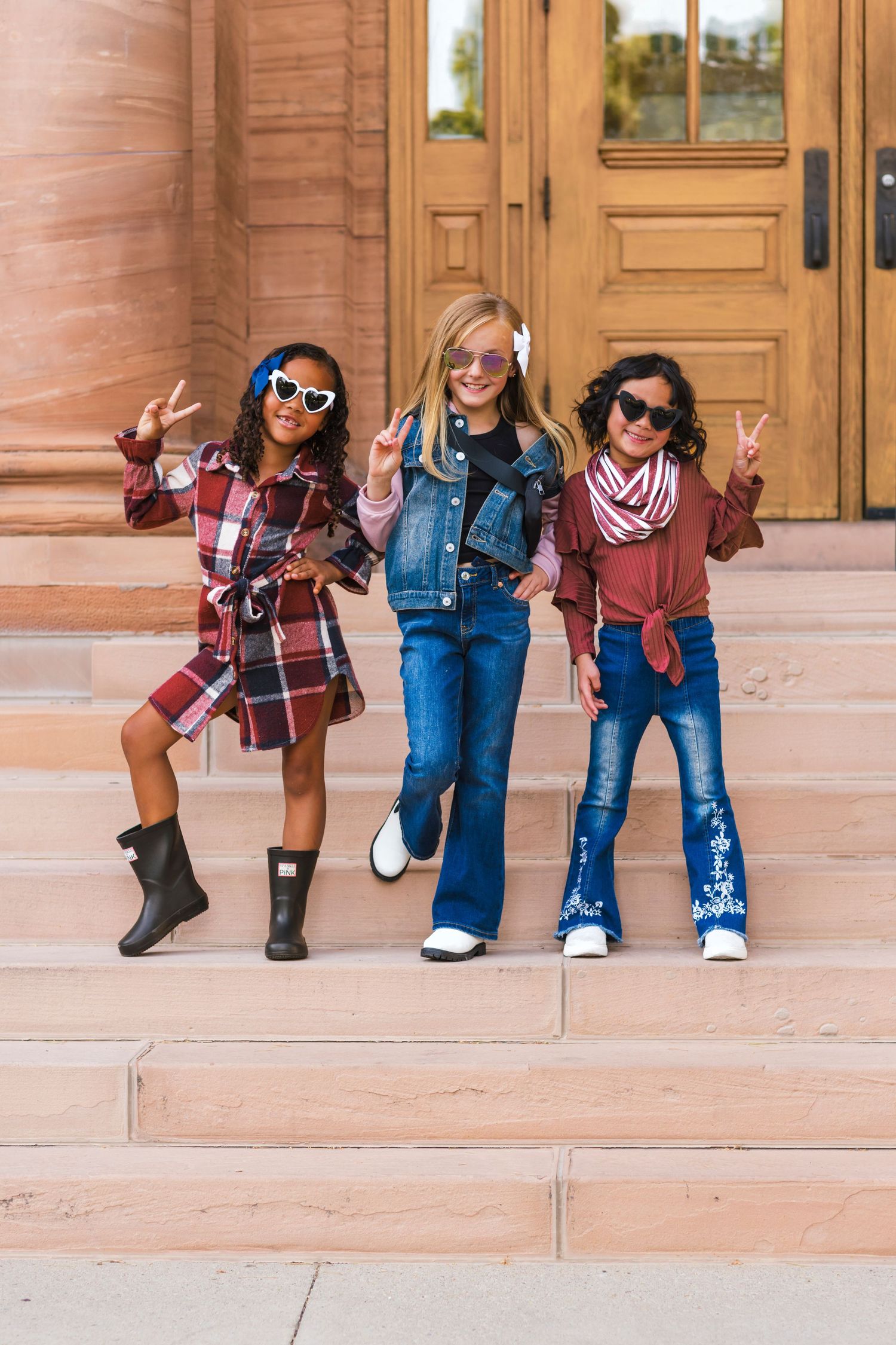 Stylish group in plaid shirts and jeans showing off their legs in professional portrait on sandy stone steps.
