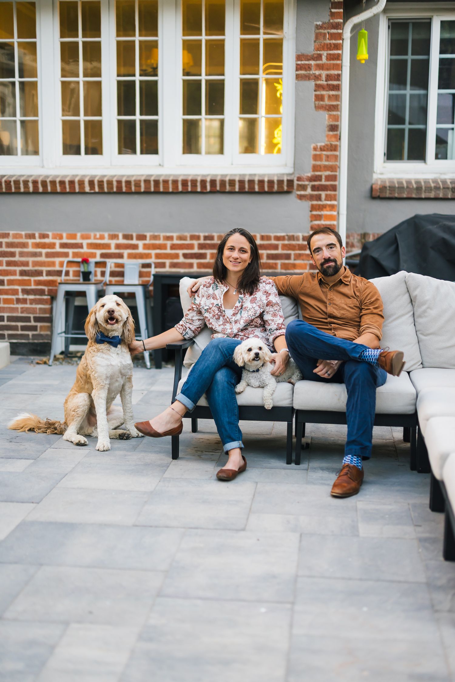 Family relaxing on outdoor patio furniture with two dogs on a stone patio.