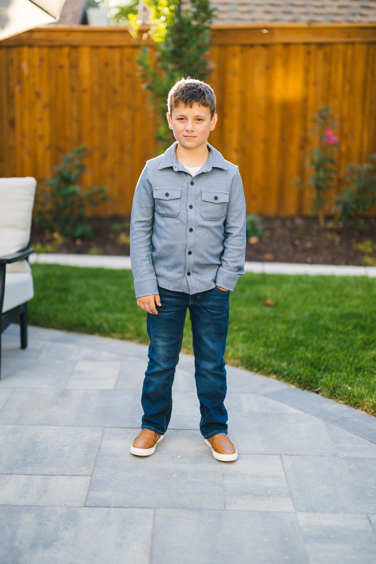 Child wearing gray jacket and jeans standing on stone patio.