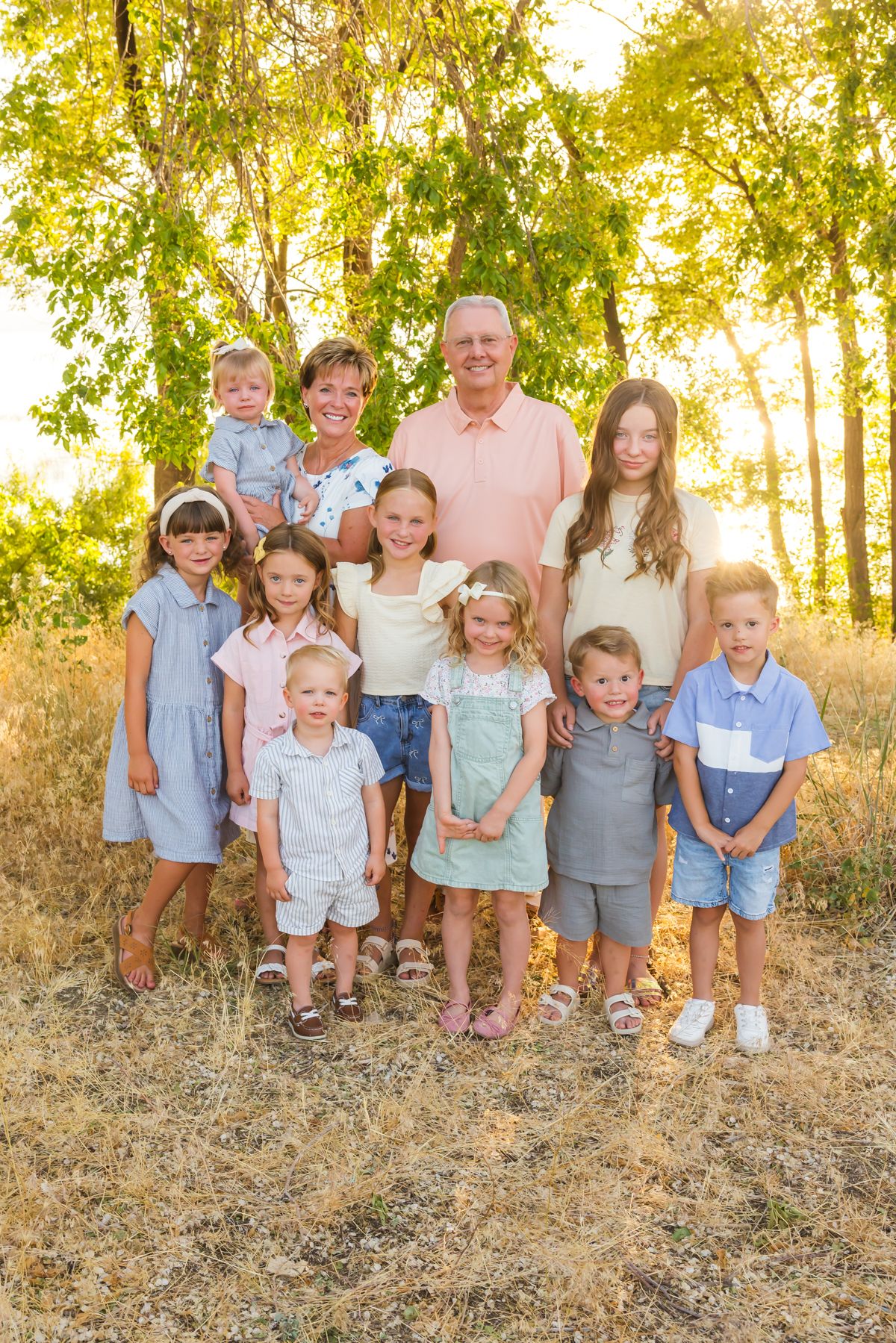 Group portrait of children with adults in coordinated outfits under sunny trees.