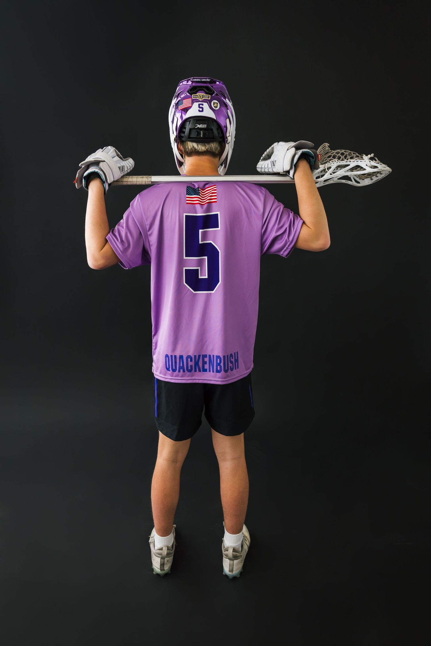 Salt Lake City senior lacrosse portrait in full uniform with stick. Back view of lacrosse player in purple jersey holding stick above head.