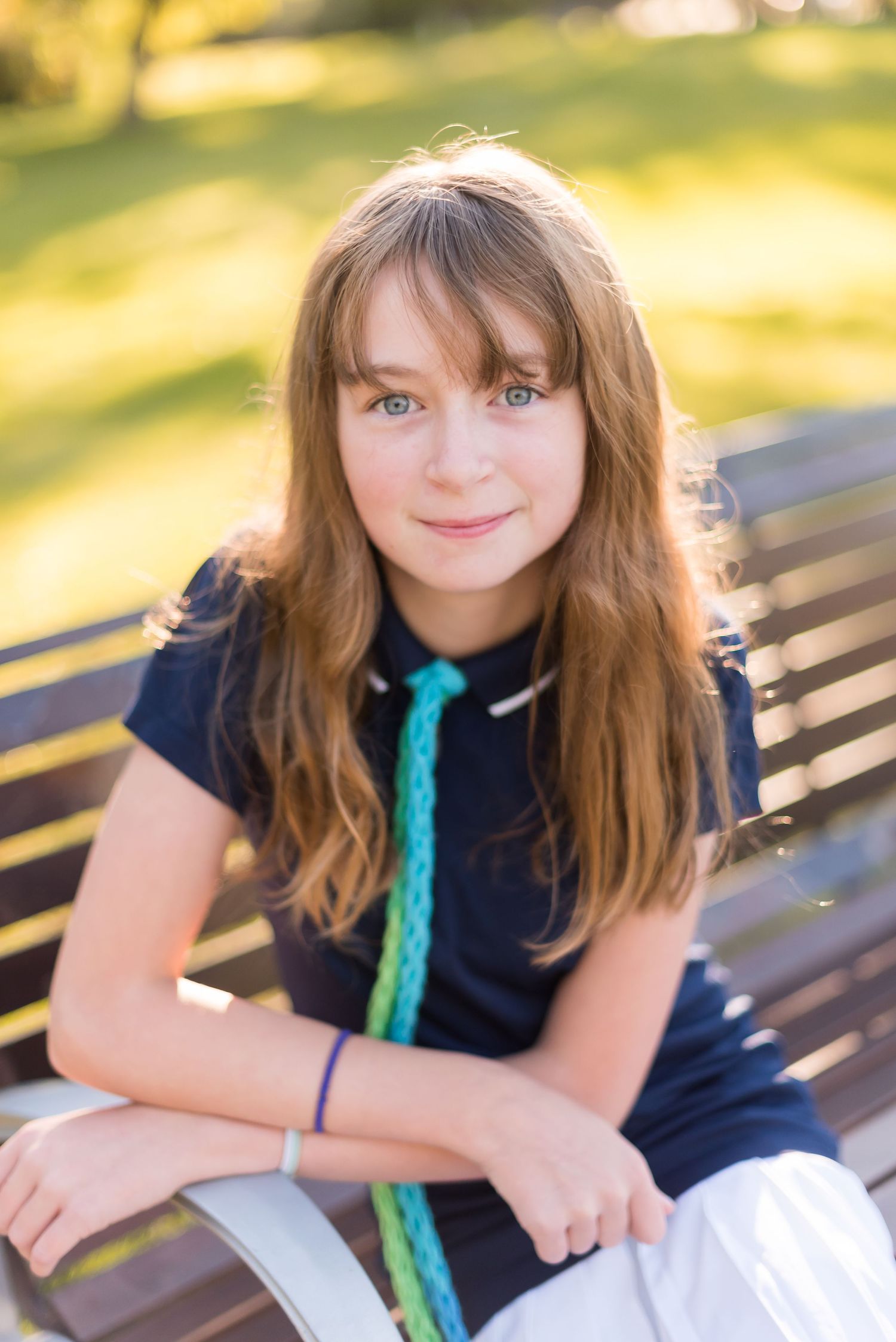 Portrait photo sitting on a wooden park bench wearing a navy blue dress with turquoise accents on a sunny day.