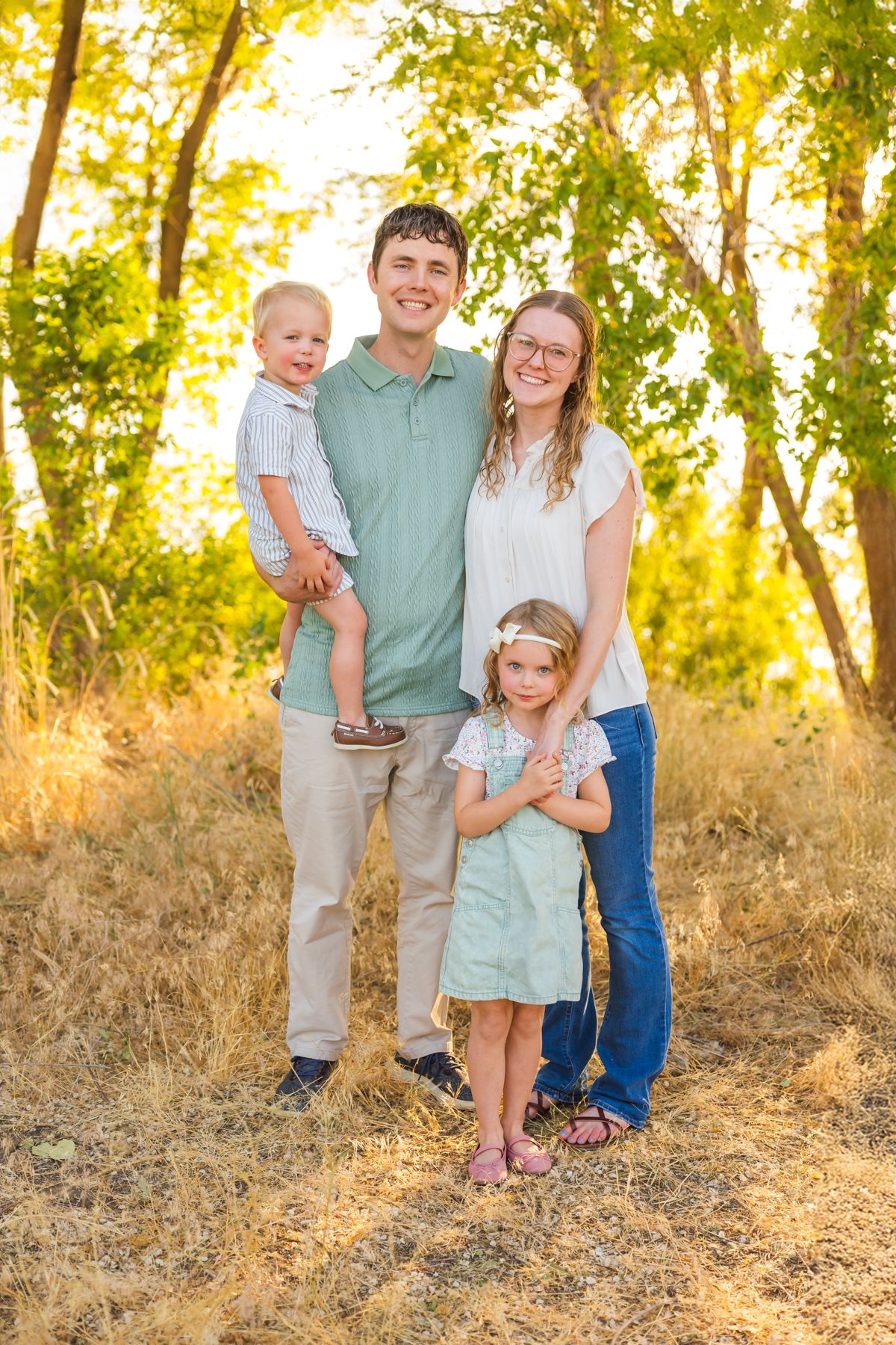 Family wearing coordinated blue and white outfits poses together in golden sunlit field during sunset.