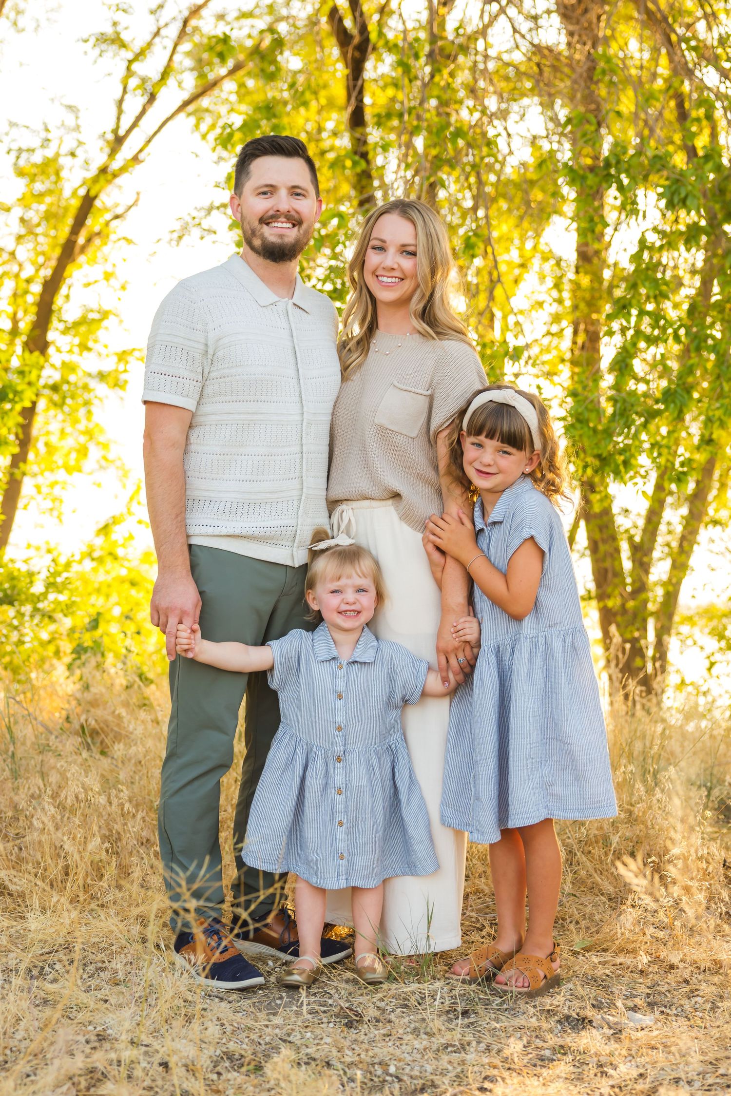 Family portrait series with coordinated blue and neutral outfits in natural outdoor setting.