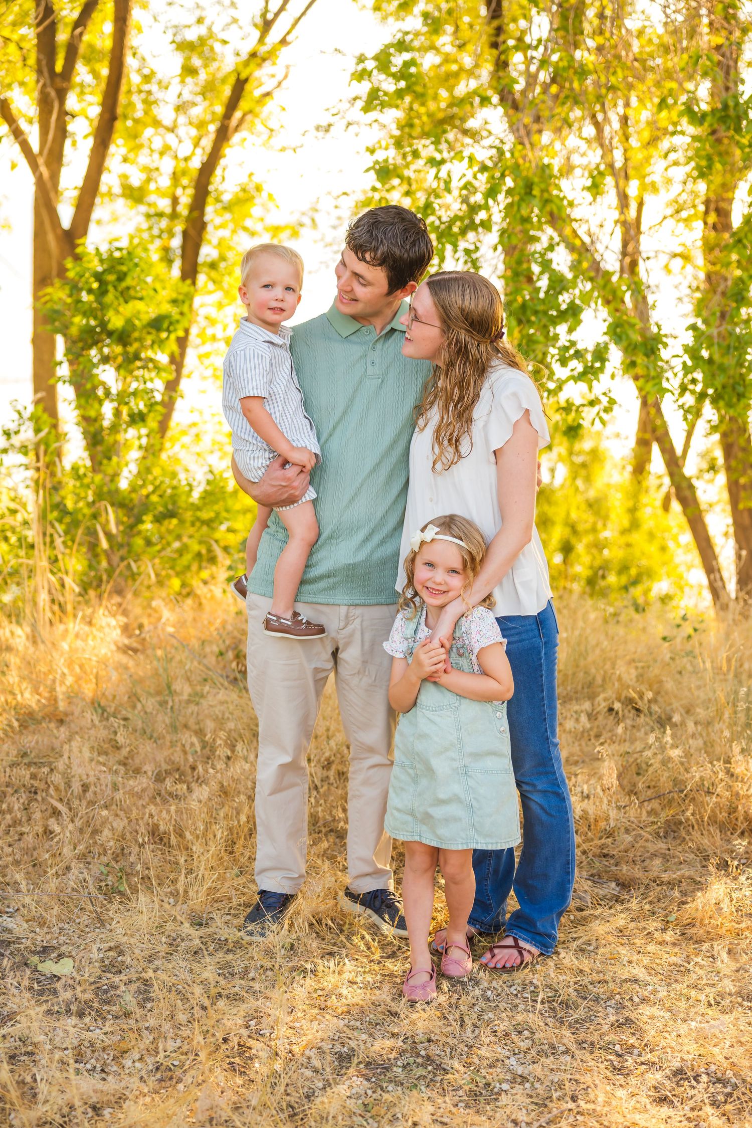 Family photoshoot in coordinated outfits against golden sunset and trees.