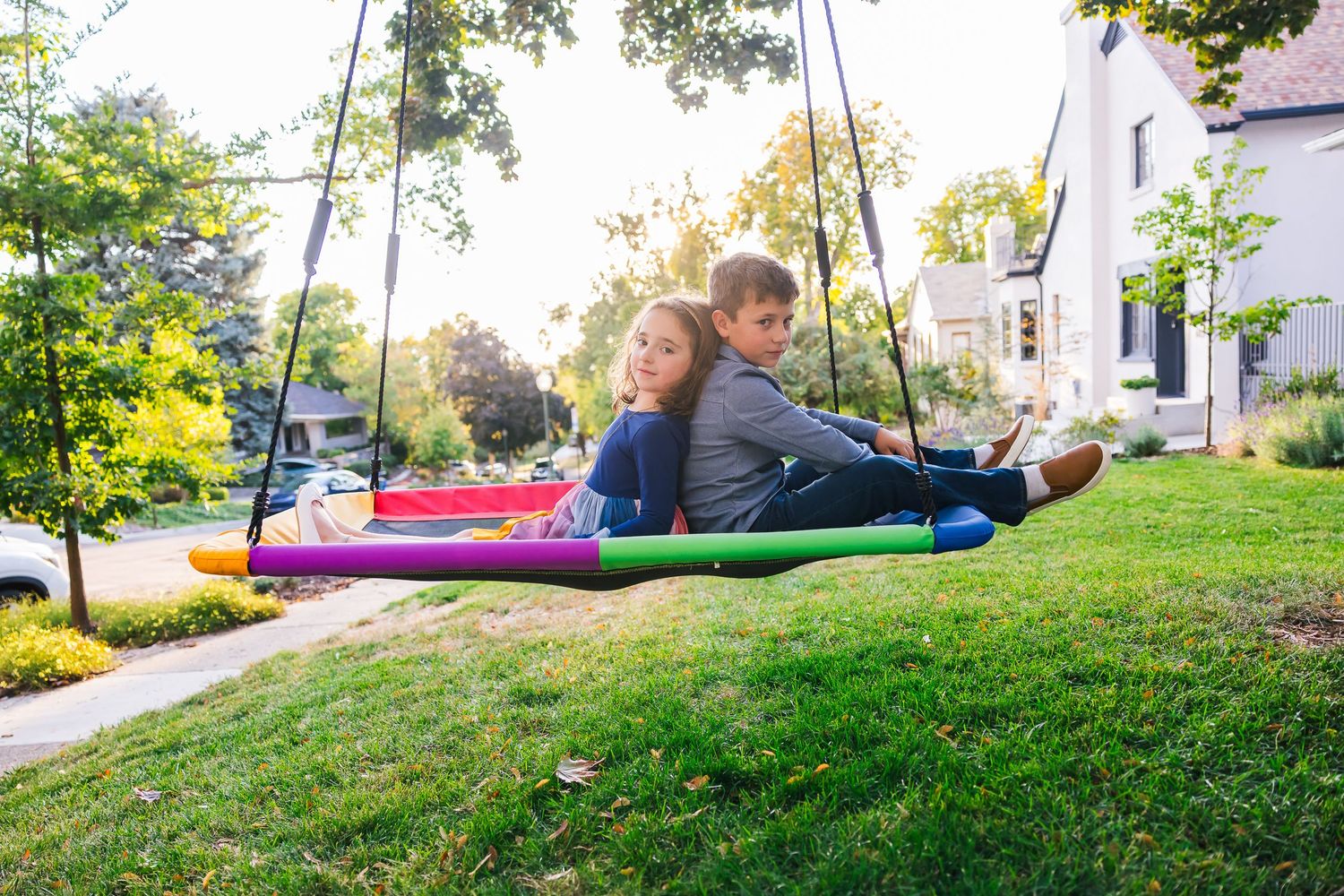 Two people enjoying a relaxed moment on an outdoor swing set in a sunny backyard.