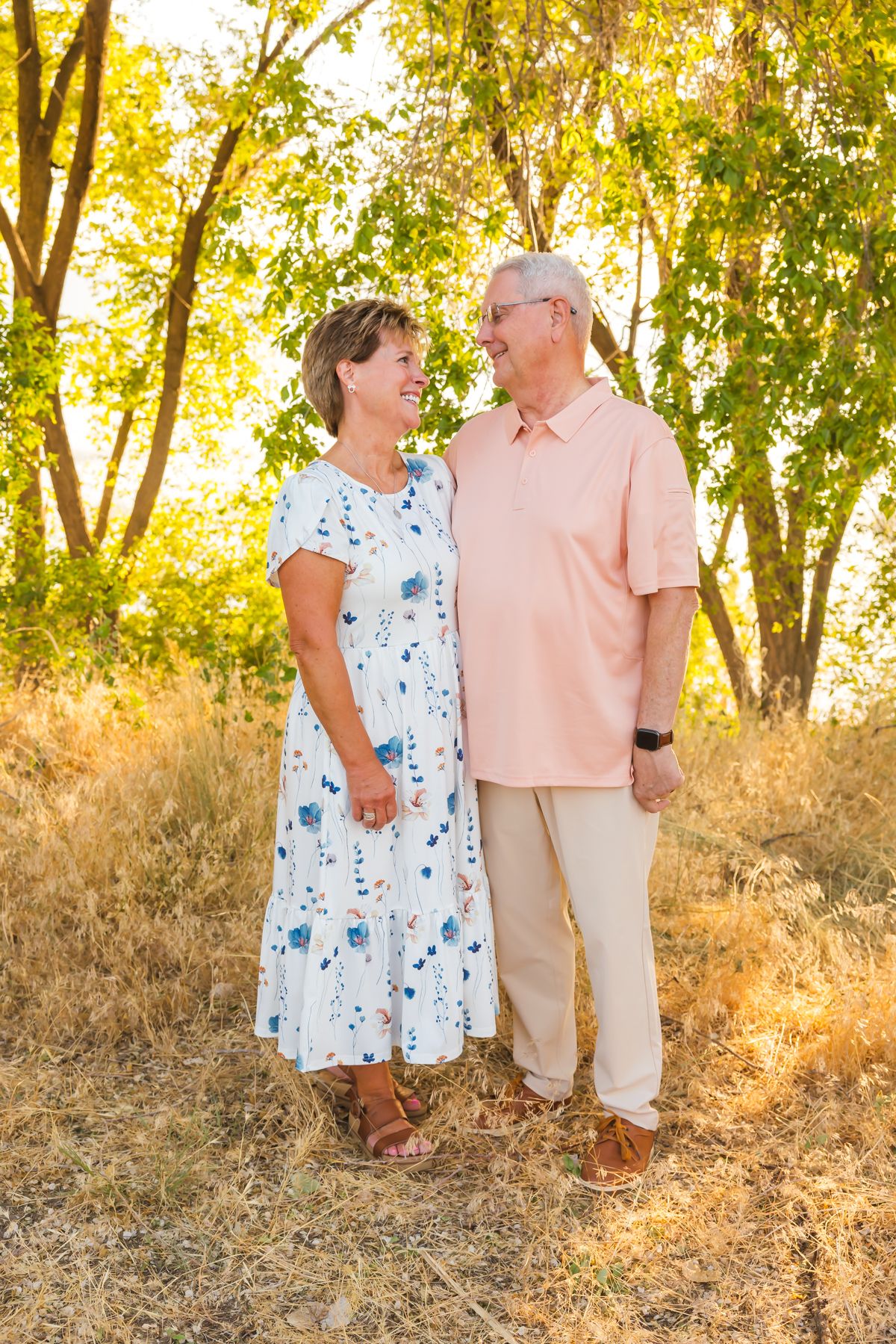 A couple poses together in a sunny outdoor setting with autumn trees and golden light.