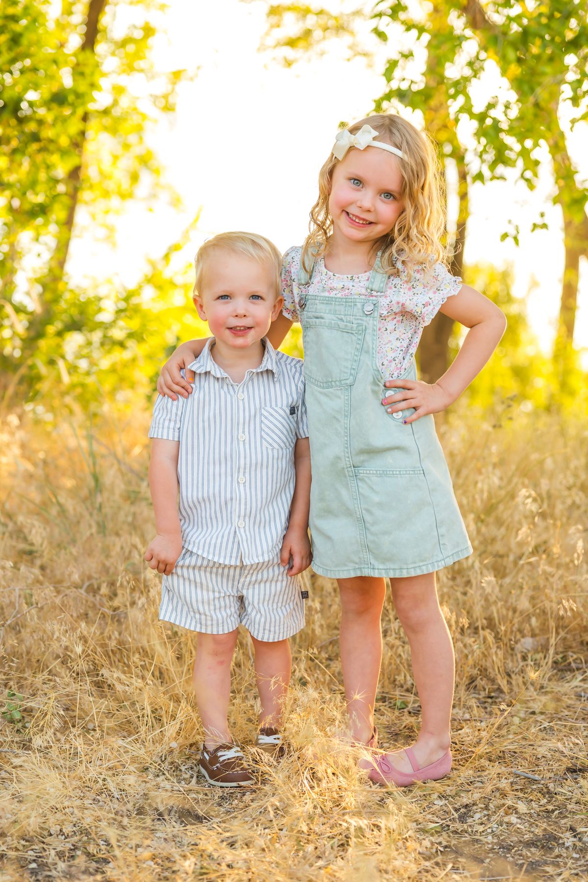 Children in coordinating blue and mint outfits play together in sun-drenched field.