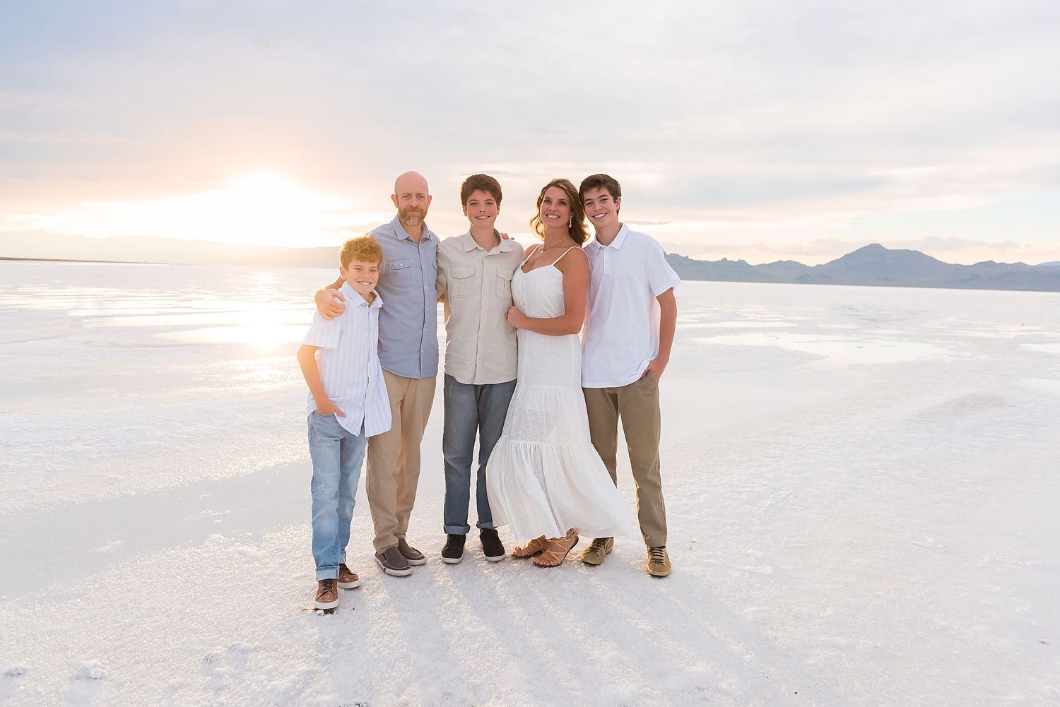 Group of people walking together at sunset on bright white salt flats with mountains in background.