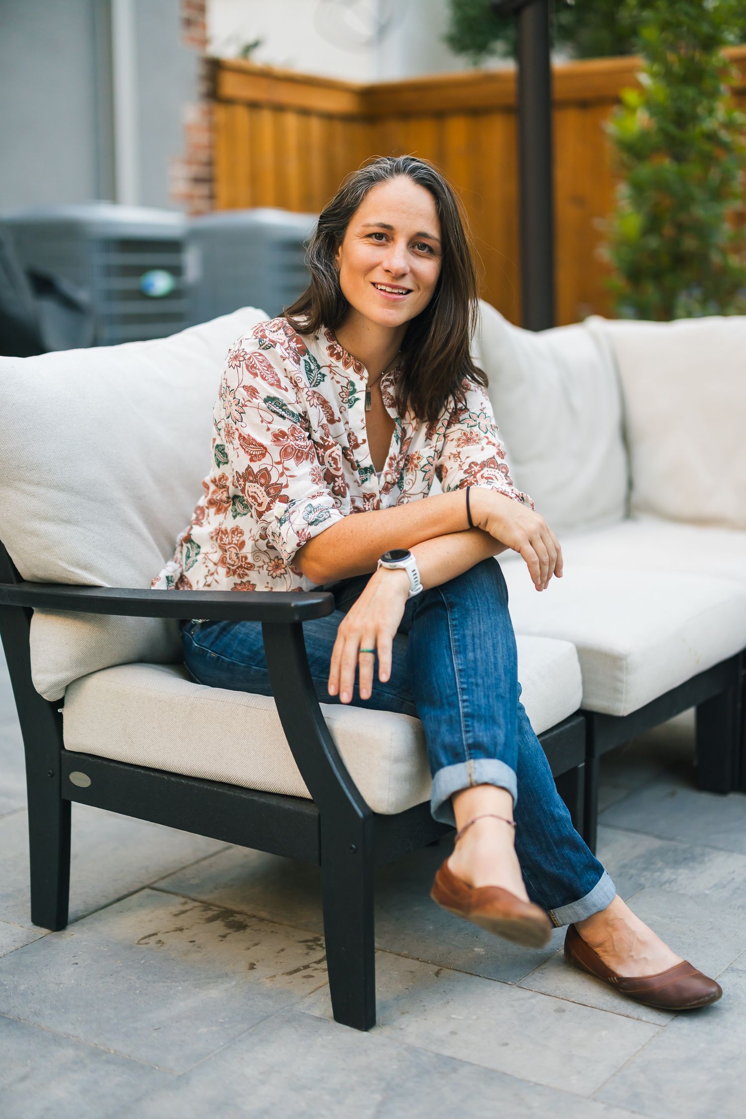 Woman in floral top relaxes on outdoor patio furniture with cushions.