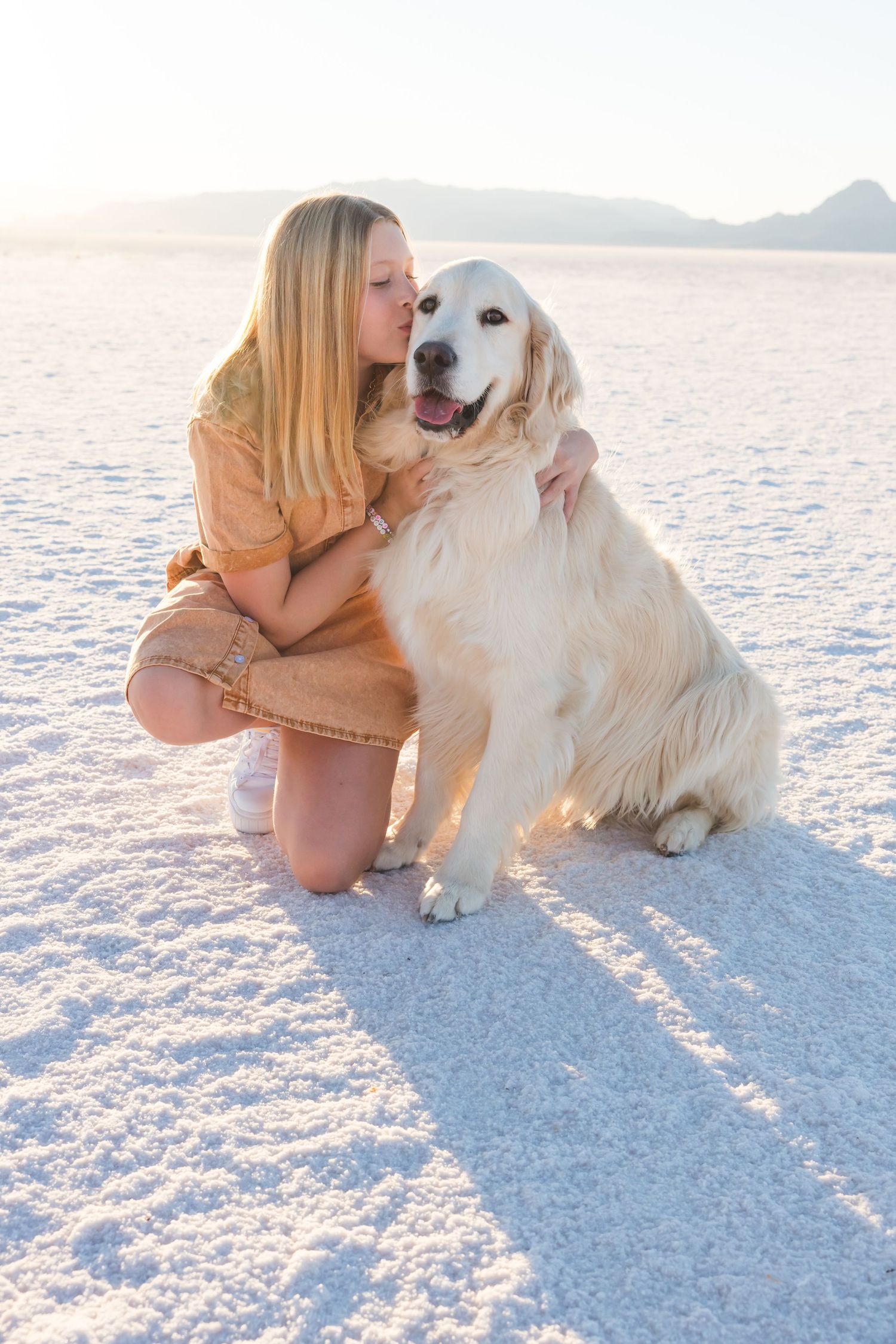 Golden retriever and person share an affectionate moment on white sand during sunset.