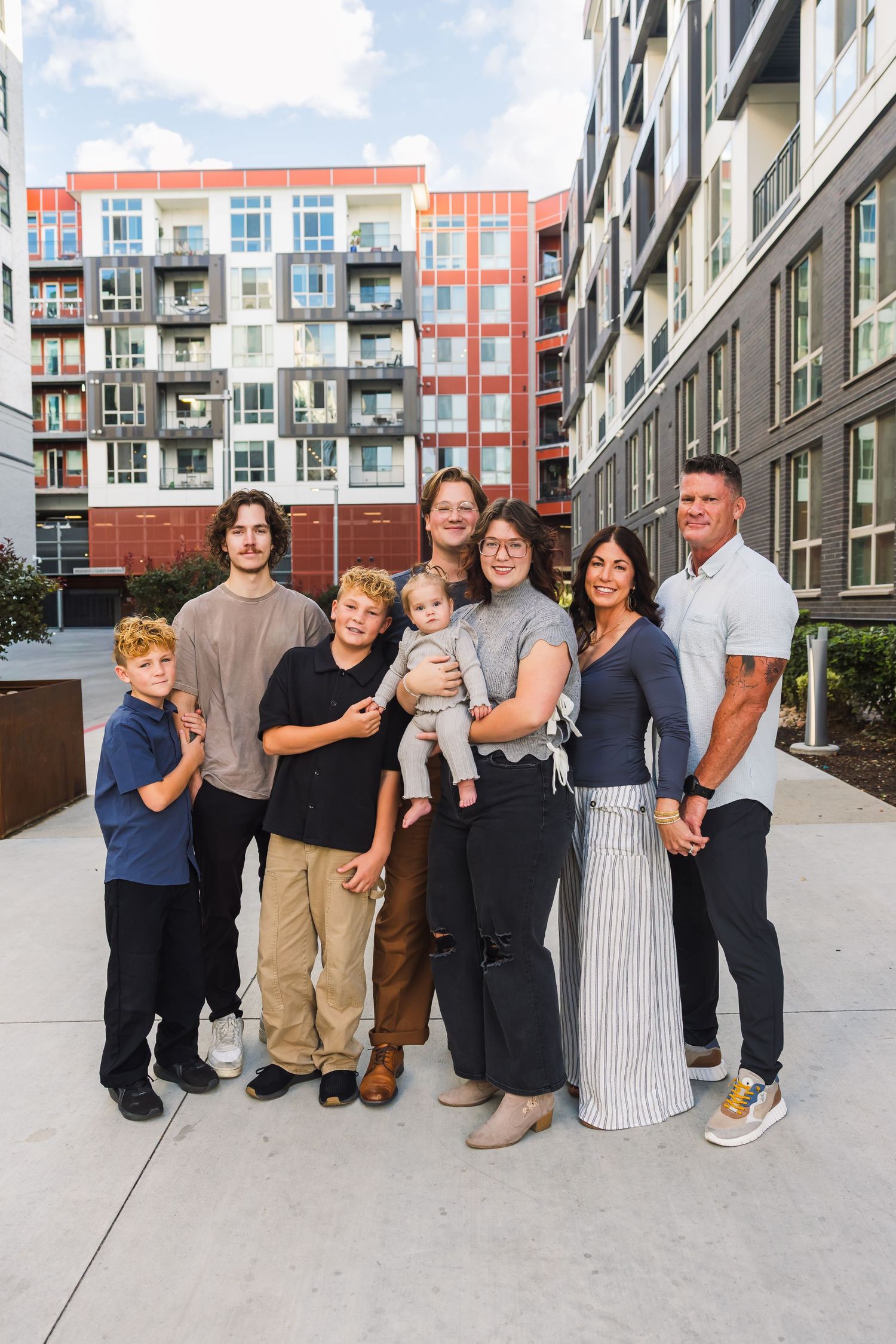 Multi-generational family group poses together on concrete walkway outside modern apartment building.