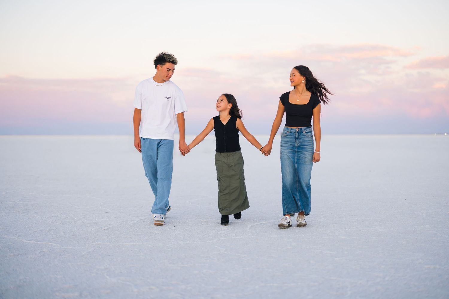 Three people walk hand-in-hand across a bright white salt flat during sunset.
