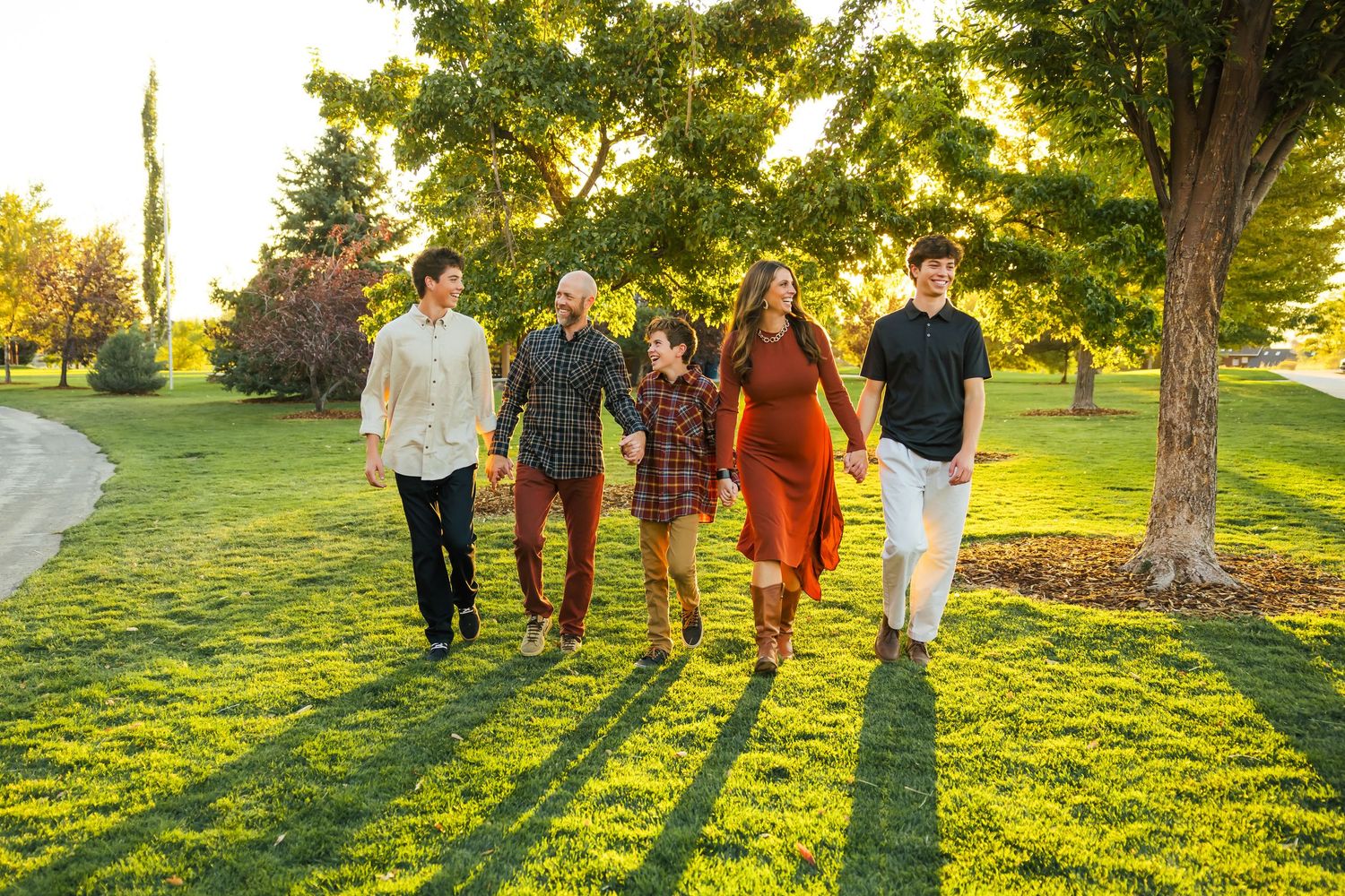 Group of people walking together across a sunlit green lawn during golden hour at sunset in a park.