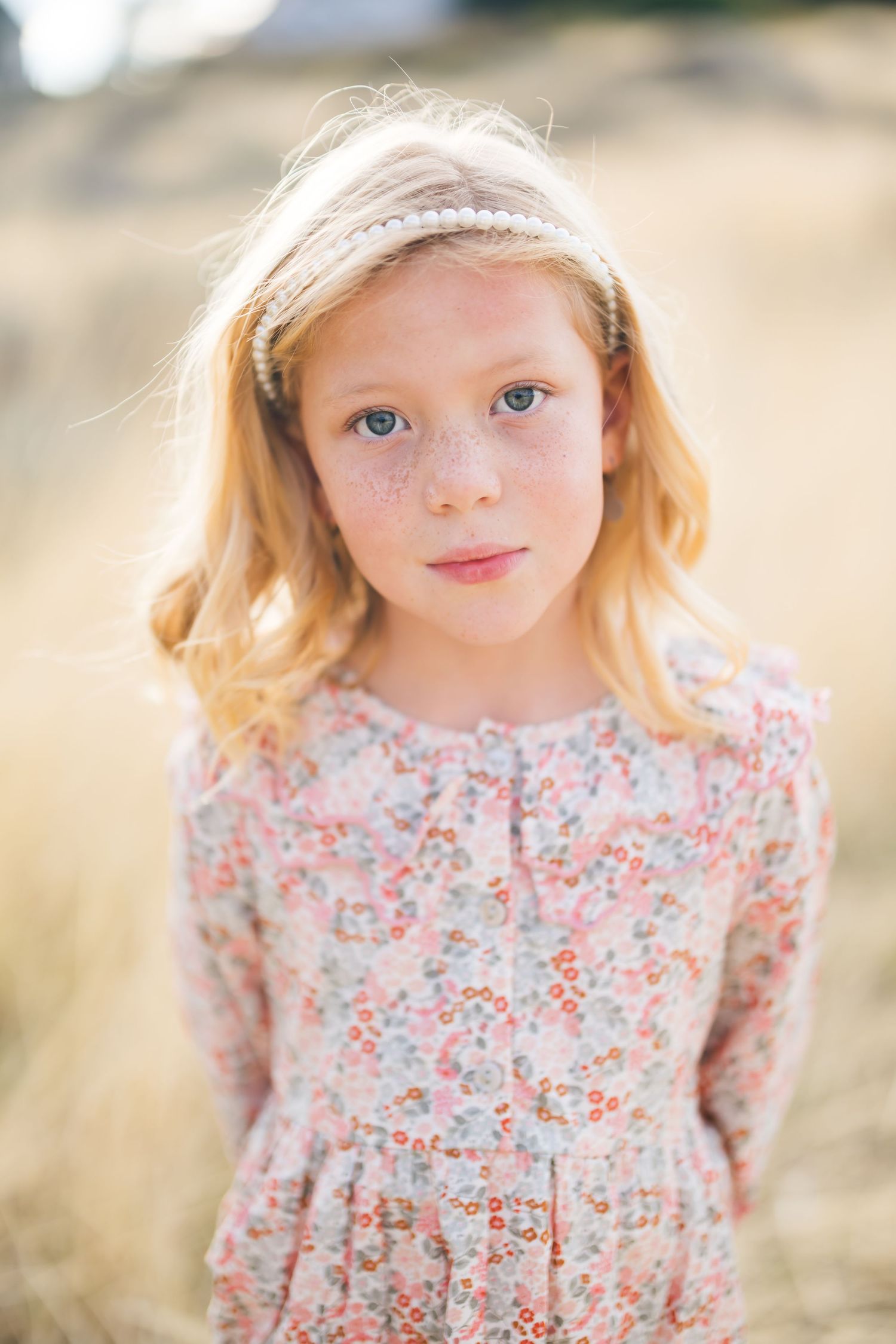 Young child wearing a floral dress smiles softly in a warm, natural outdoor setting in field in sandy utah