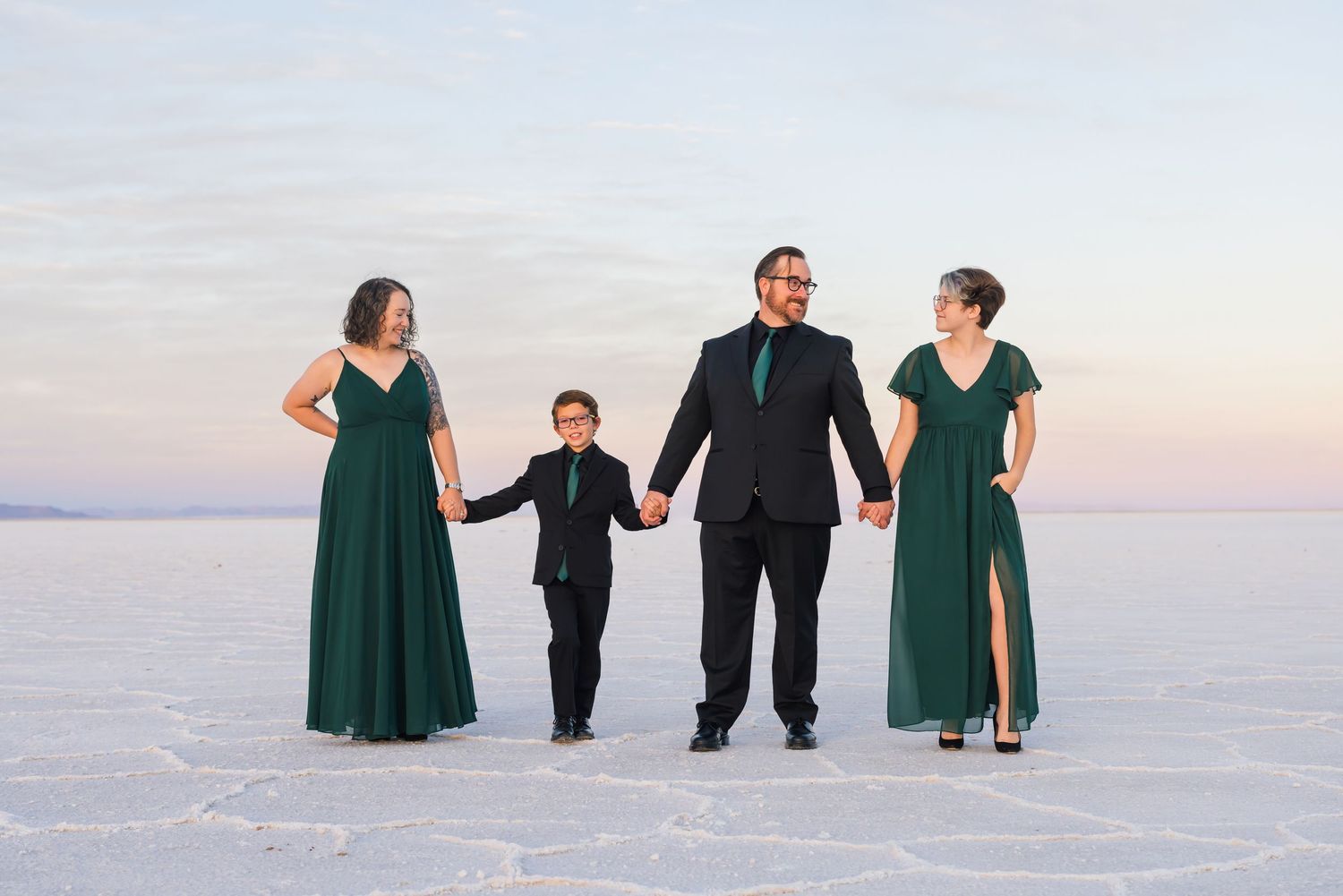 Group poses playfully on white salt flats at sunset wearing formal attire during their family photoshoot