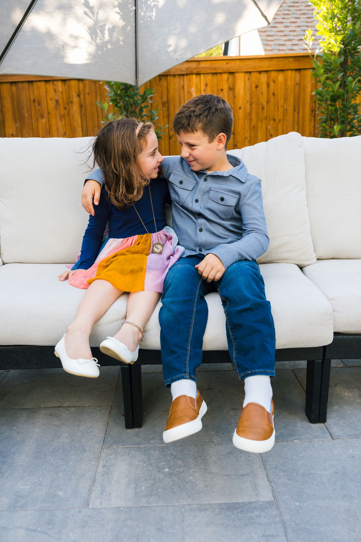 Two children sitting close together on outdoor patio furniture.