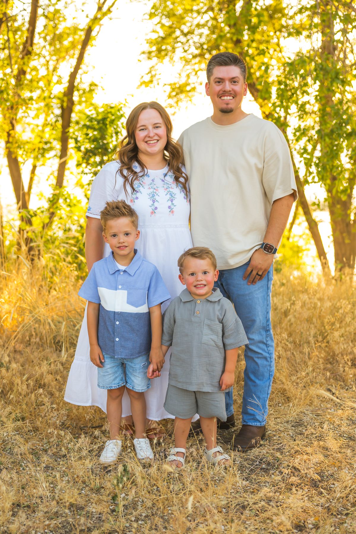 Family gathering outdoors in coordinated blue and neutral outfits during golden hour sunset.
