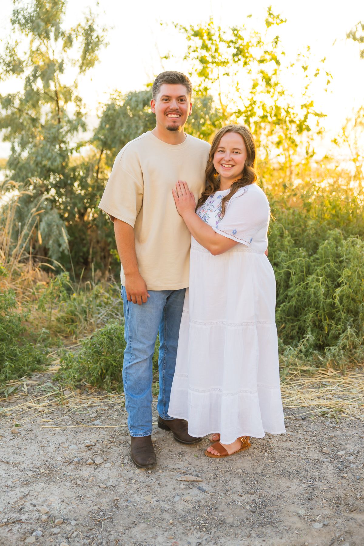 Couple in casual white outfits smiling together during outdoor sunset photoshoot.