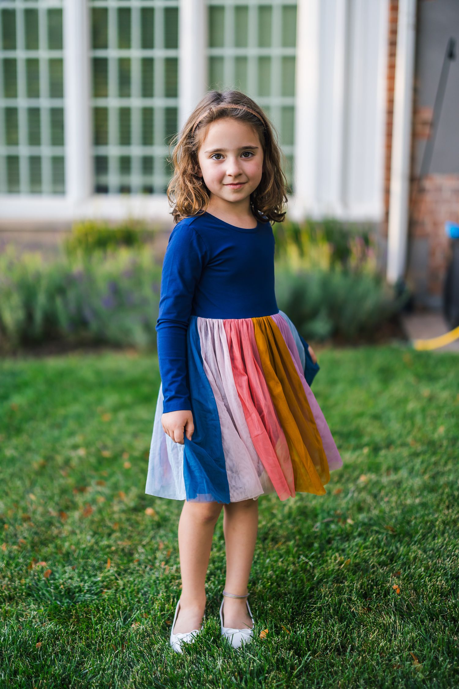 Young girl in a blue dress with colorful rainbow skirt twirls on the lawn.