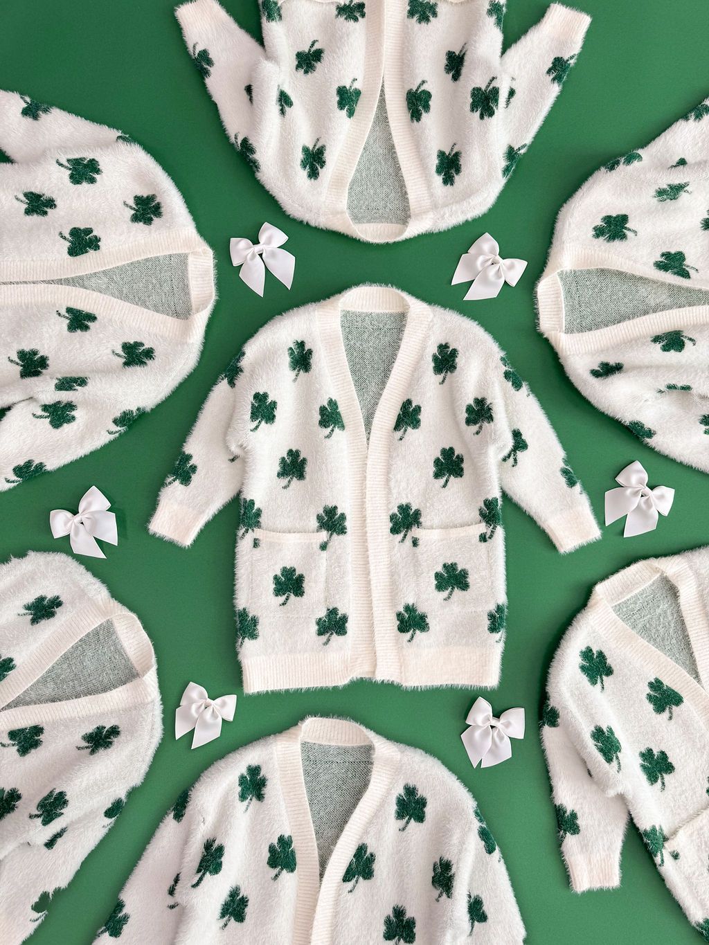 White baby onesies with green shamrock patterns displayed on green background.