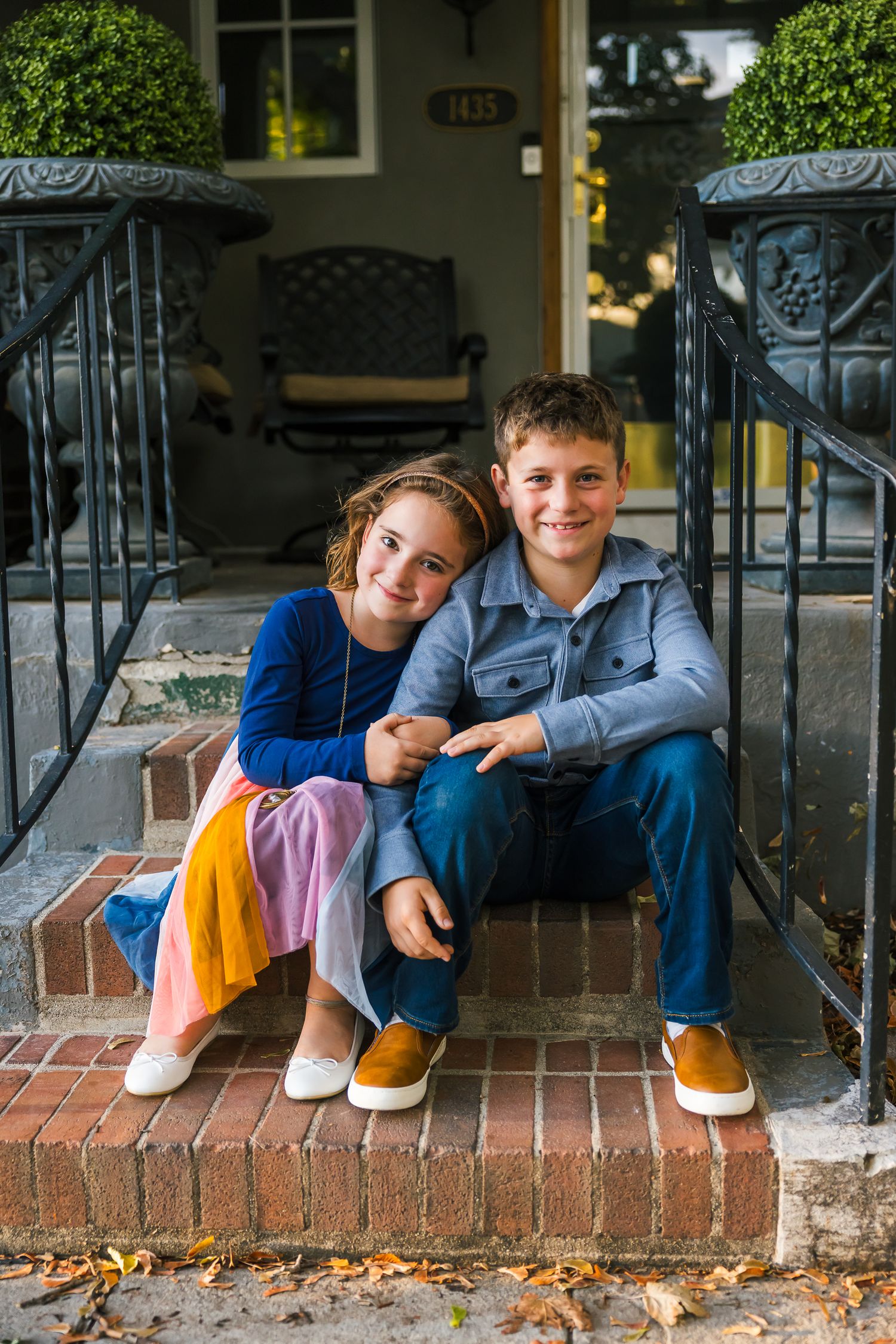 Two children sit together on brick porch steps sharing a sweet sibling moment.