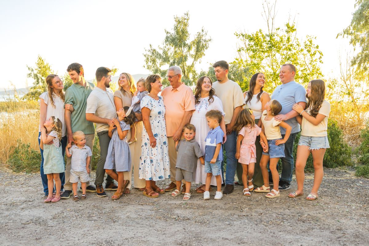 Large extended family gathering poses for outdoor photo in casual summer attire during golden hour.