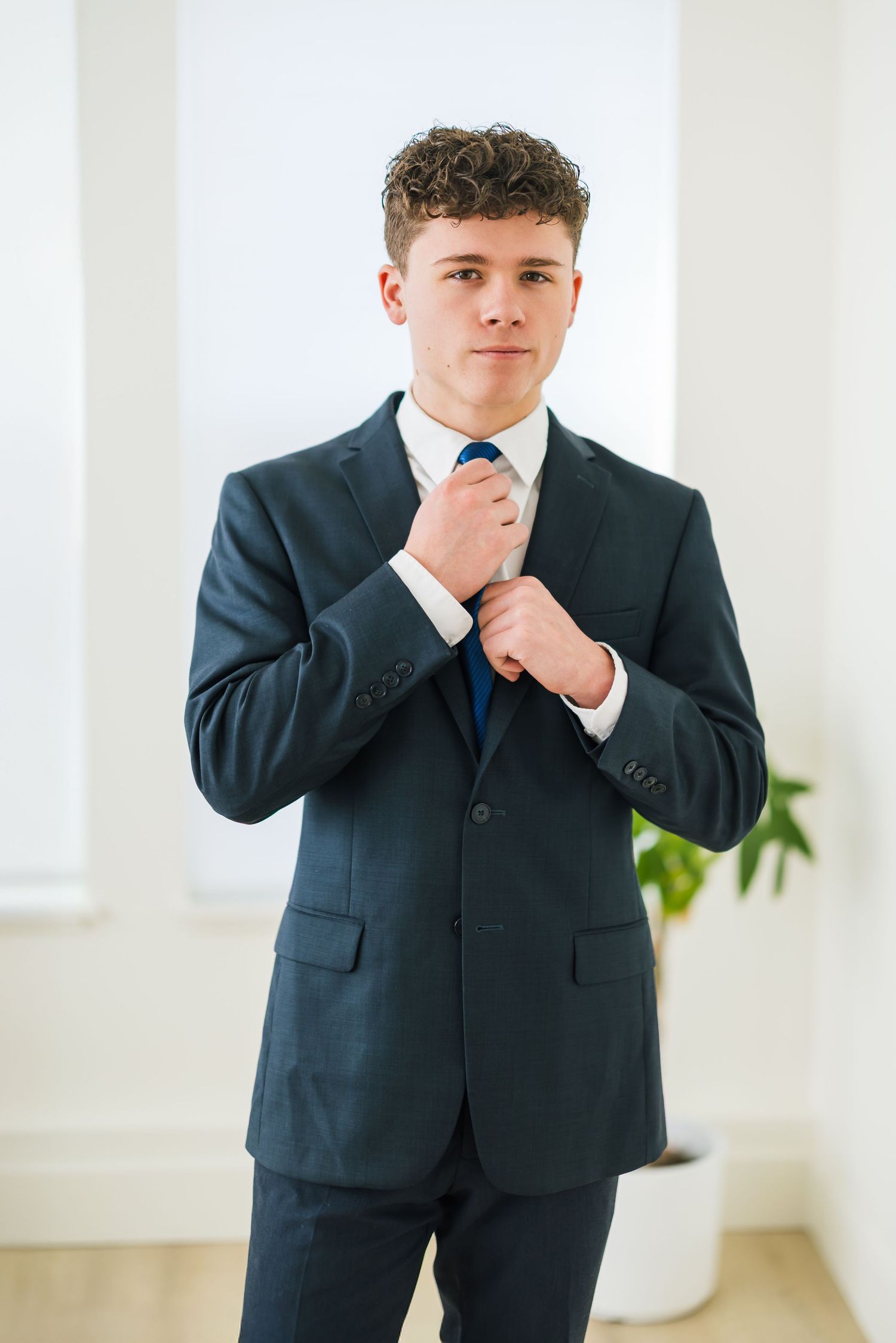 Portrait series showing senior boy adjusting tie while wearing dark business suit utah senior photography