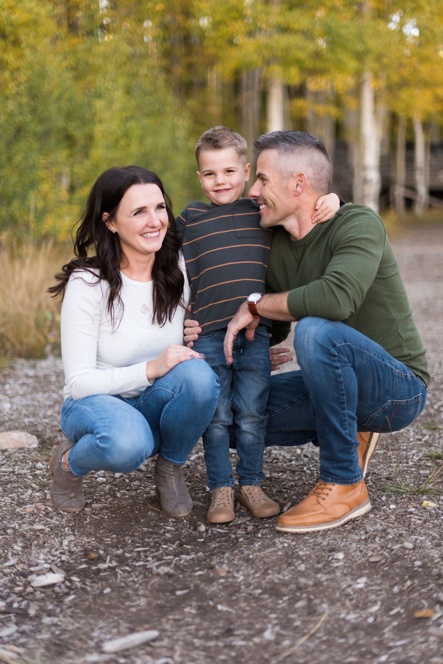 Family in casual clothing poses together on a forest path during autumn with yellow foliage in background.