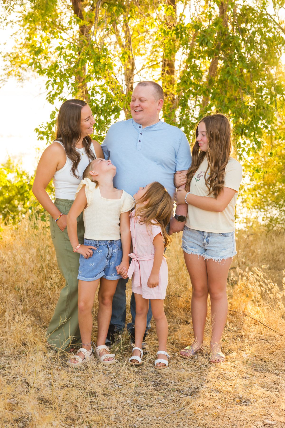 A family of five laughs together during an outdoor photo session in golden evening light.