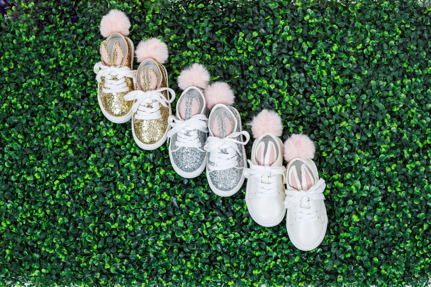 White baby shoes arranged in a row against a green leafy background for a creative newborn photography display.