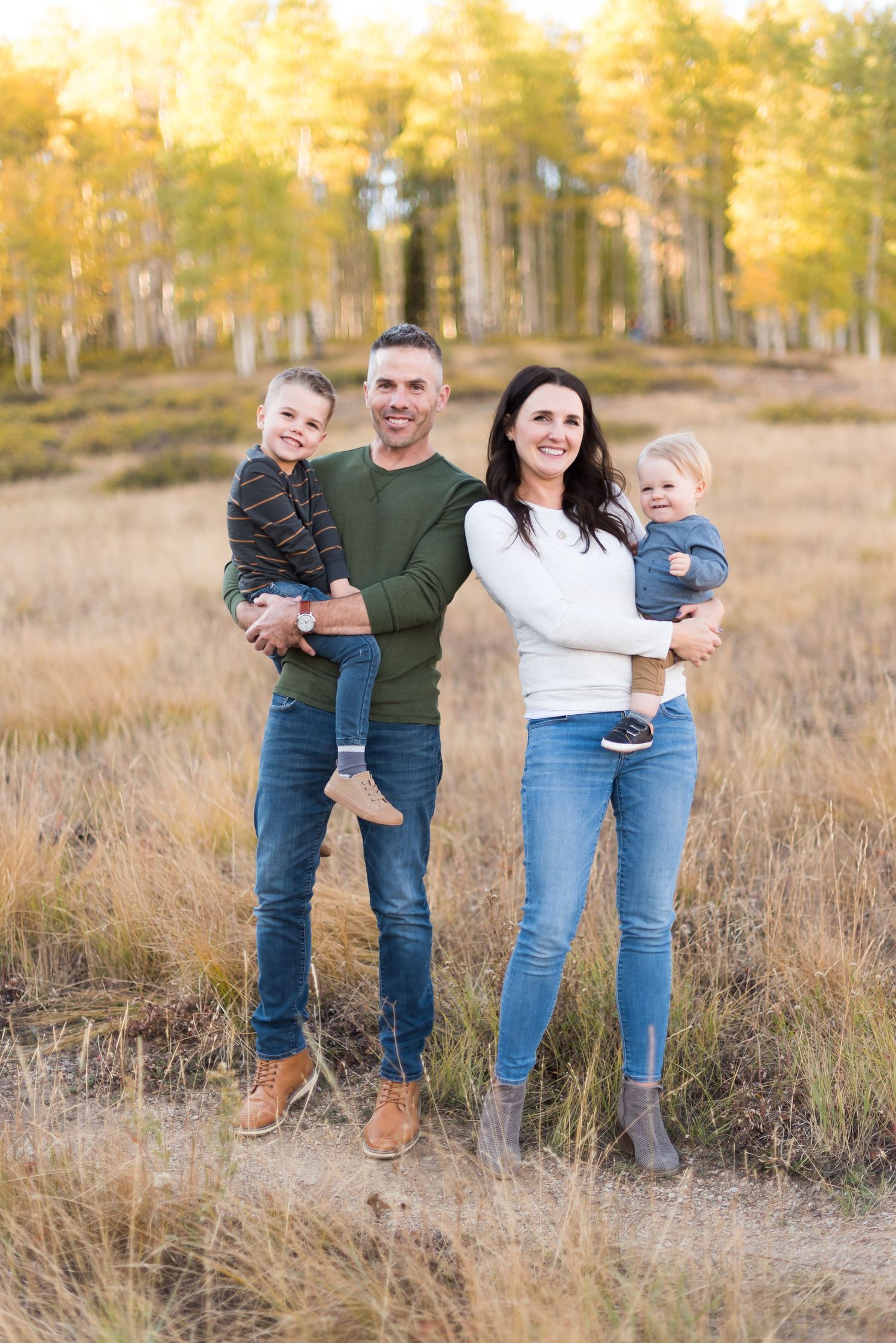 A family wearing casual clothing poses together in a golden autumn field during sunset.