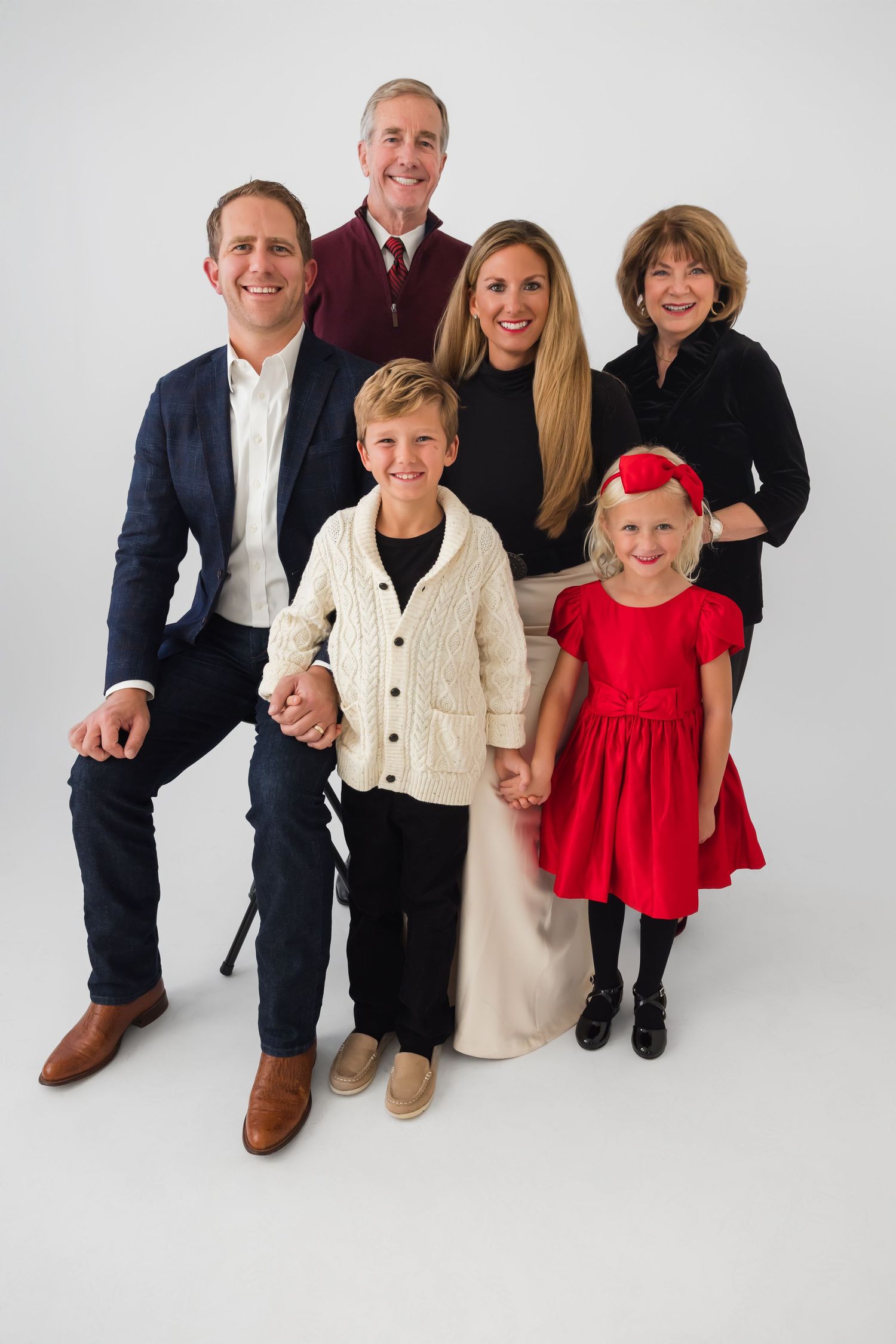 Multi-generational family portrait in studio setting with white background wearing coordinated formal attire.