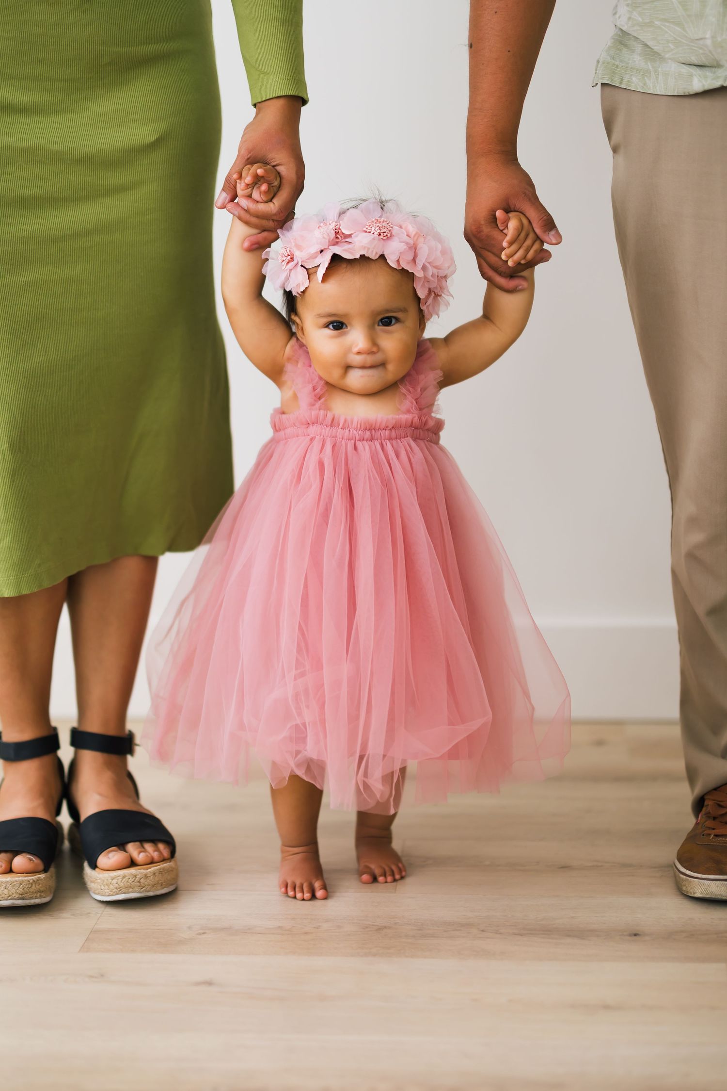 A sequence of photos showing tiny feet in a pink tulle tutu dress next to adult legs on a light wood floor.