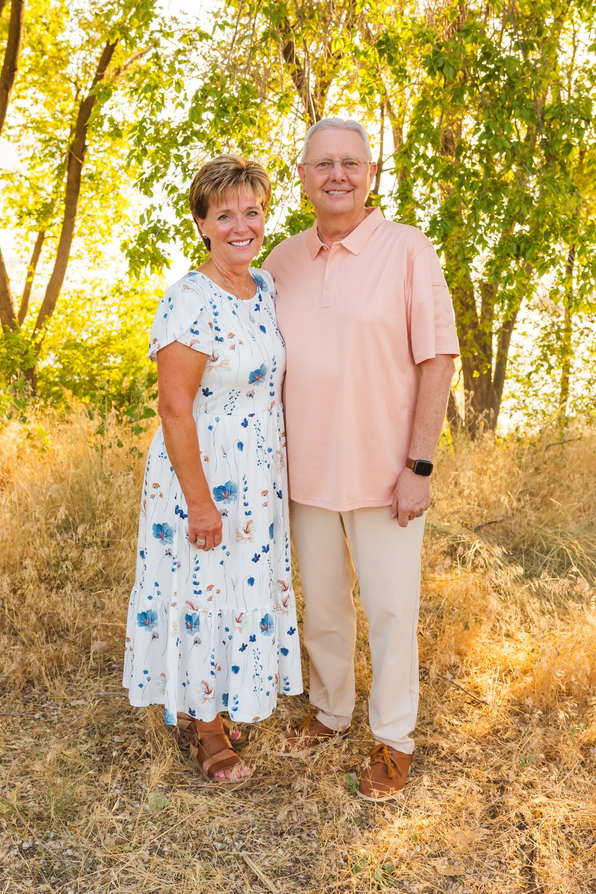 Couple in casual attire posing together outdoors during golden hour.