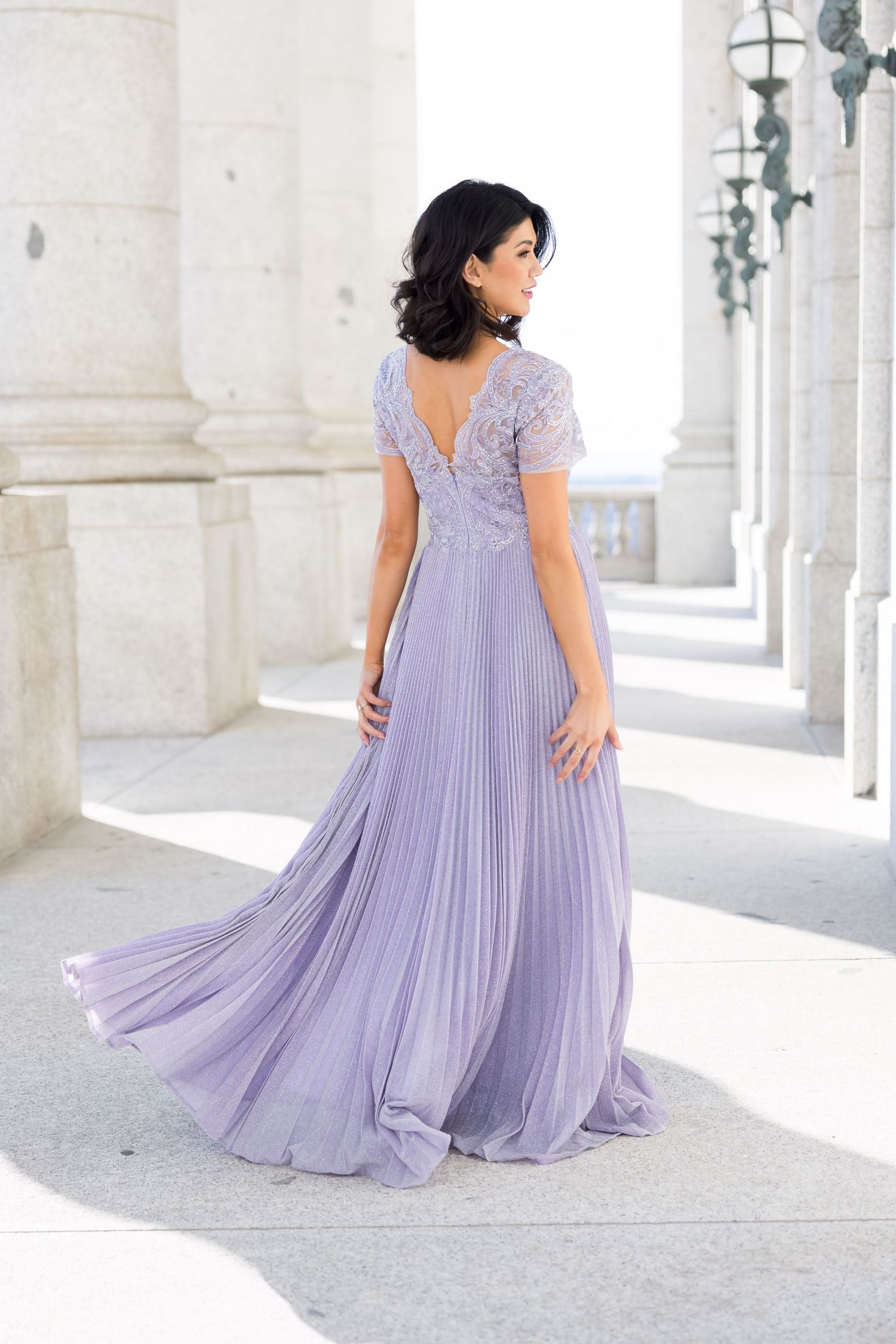 Elegant flowing lavender dress photographed in a bright white colonnade with classical architecture.