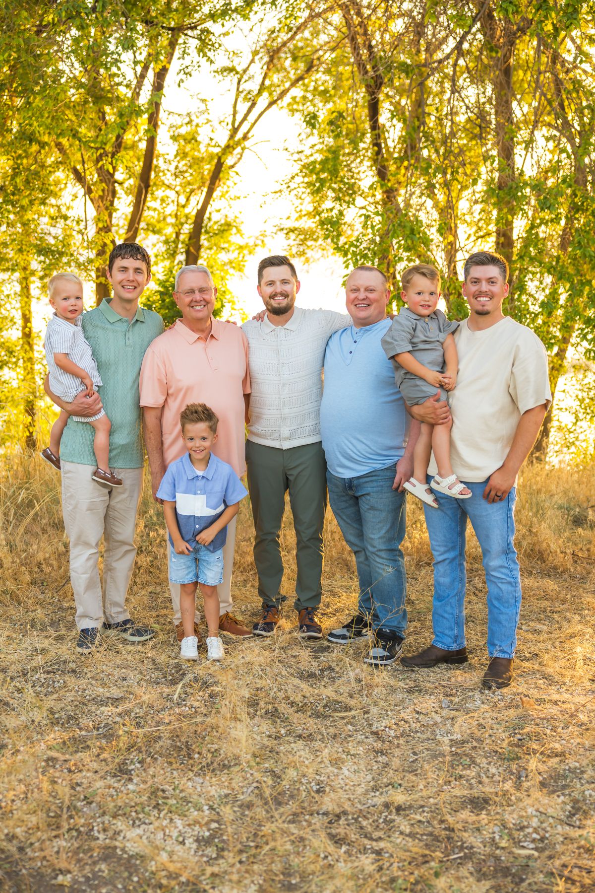 Multi-generational family group poses together on a hillside at sunset with trees in background.