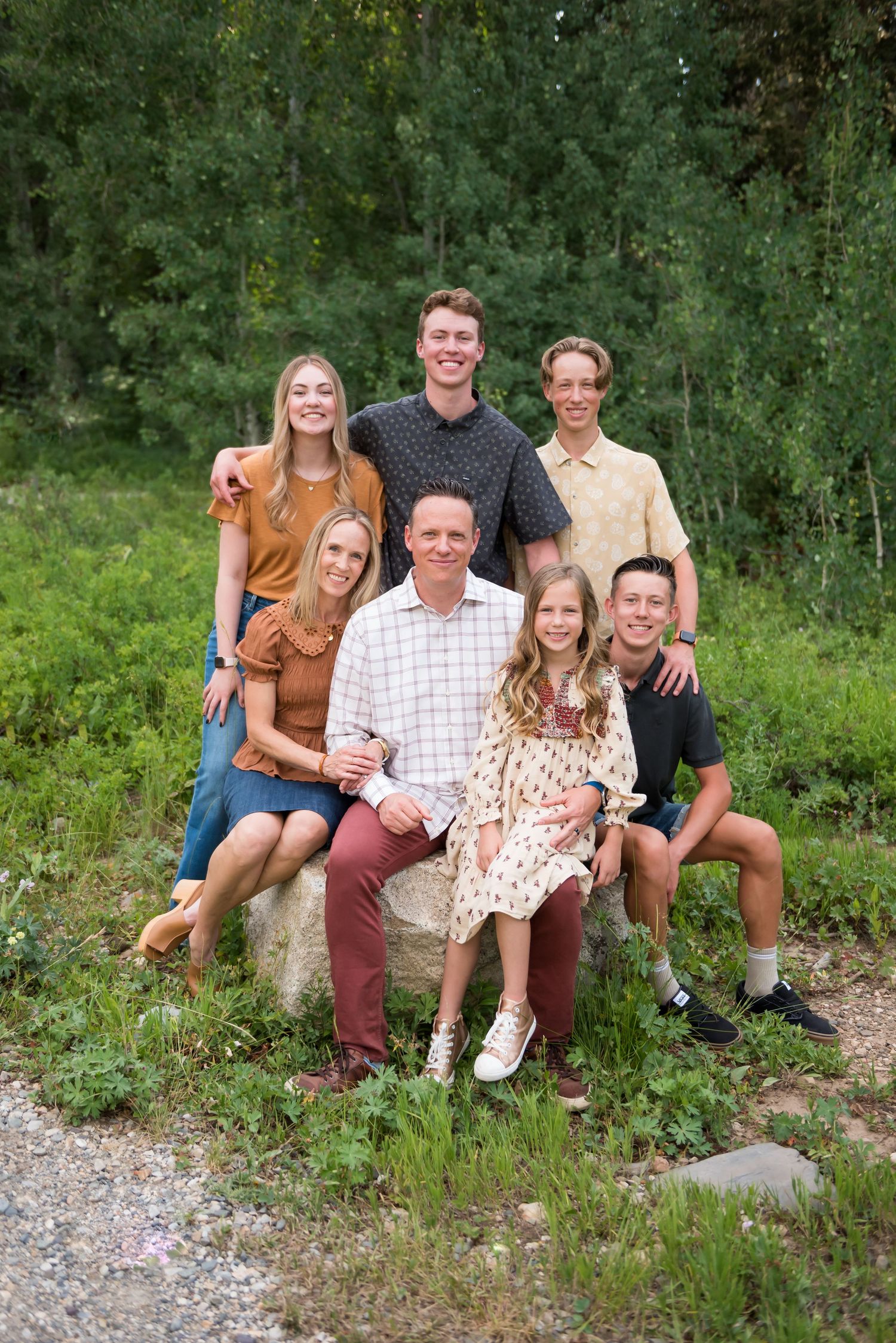 A group of six people pose together outdoors on a hillside with green foliage in the background.