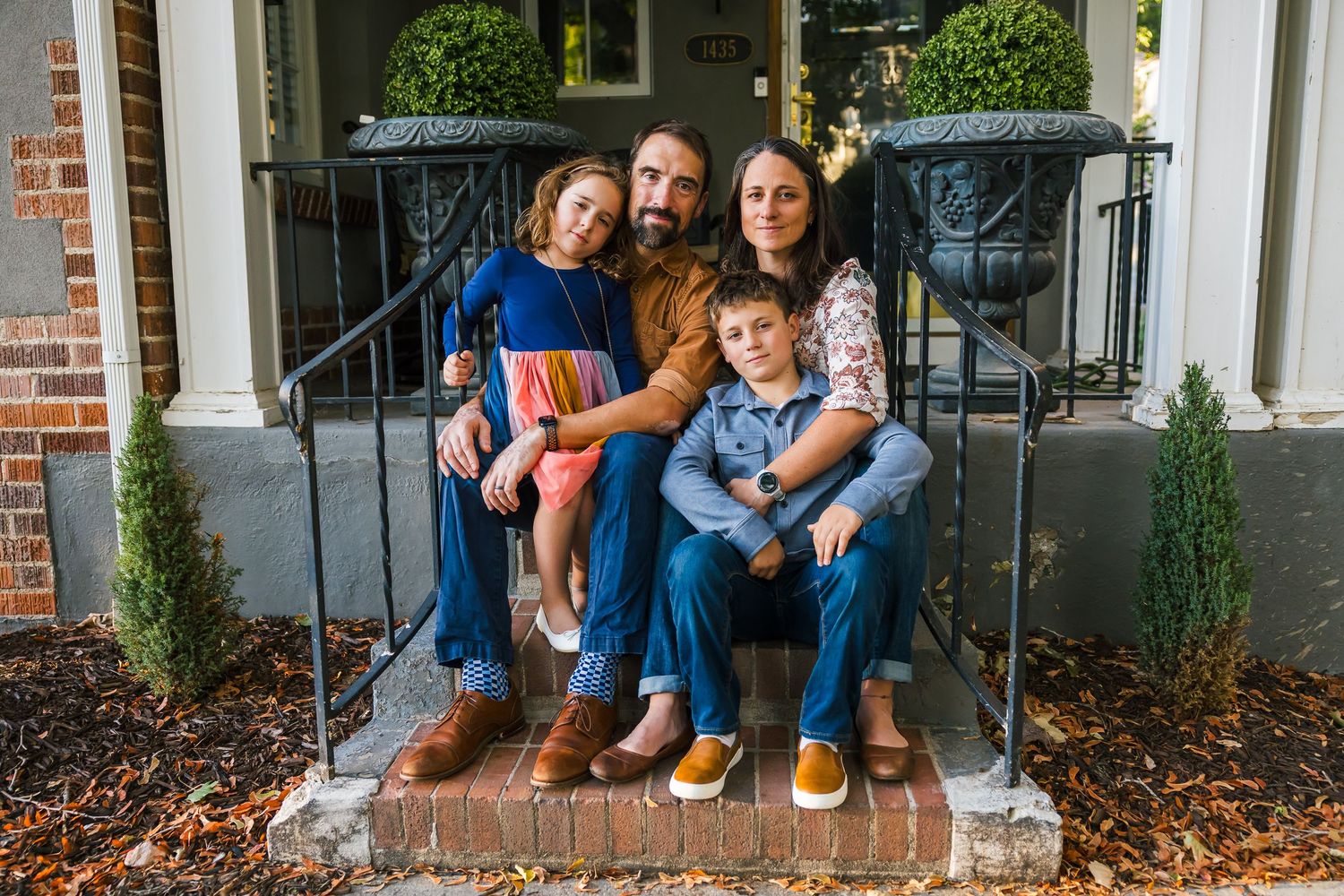 A family sits close together on brick front porch steps for a casual portrait.