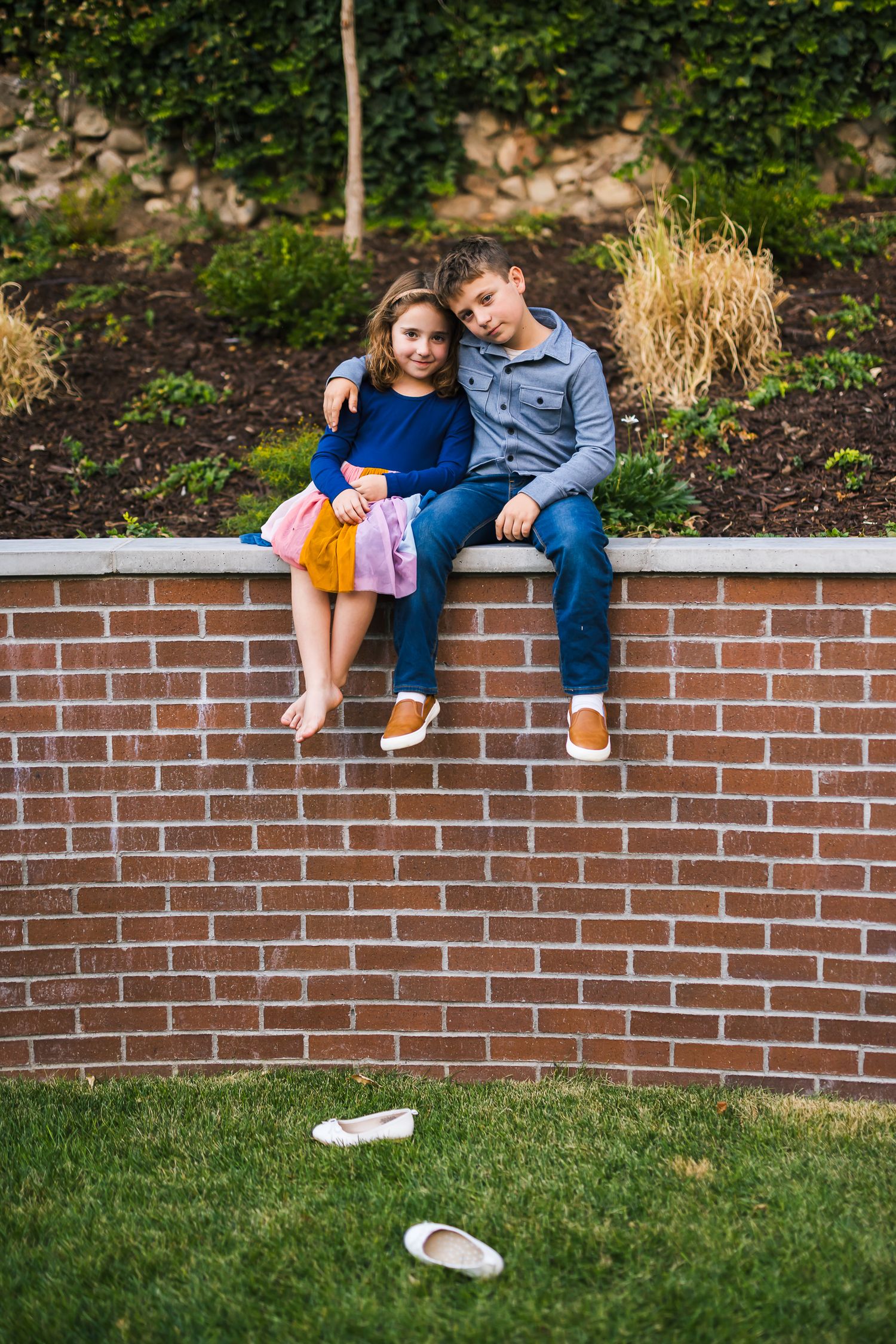 Couple sitting intimately on brick retaining wall with shoes kicked off below.