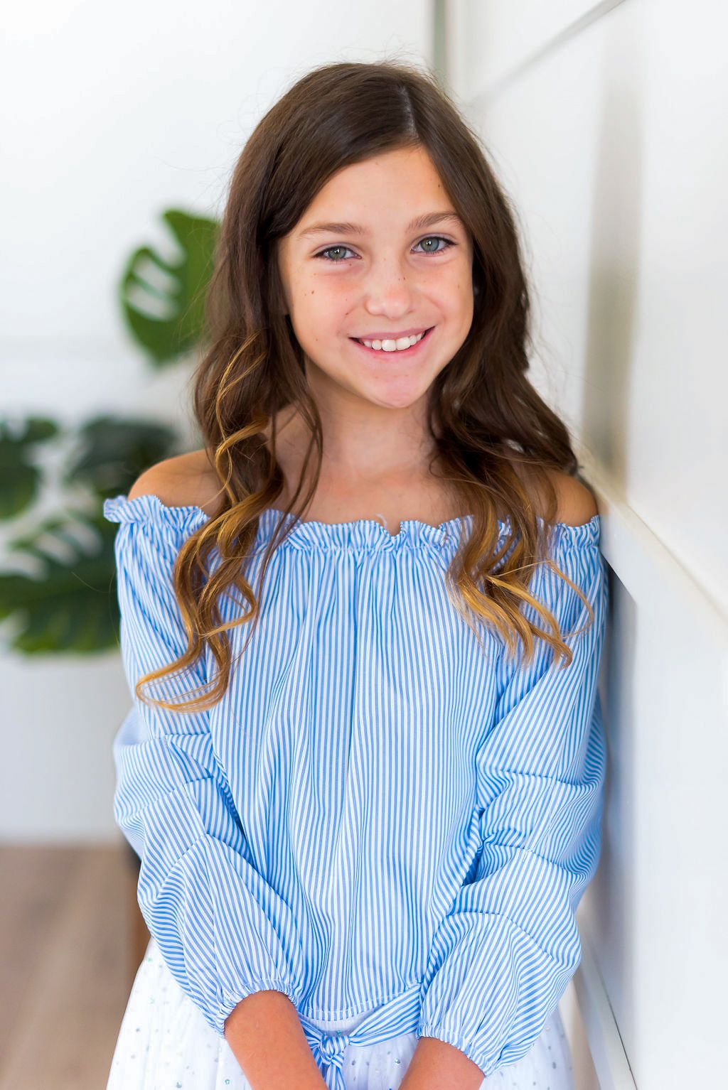 Young person in blue and white striped off-shoulder top smiling at camera.