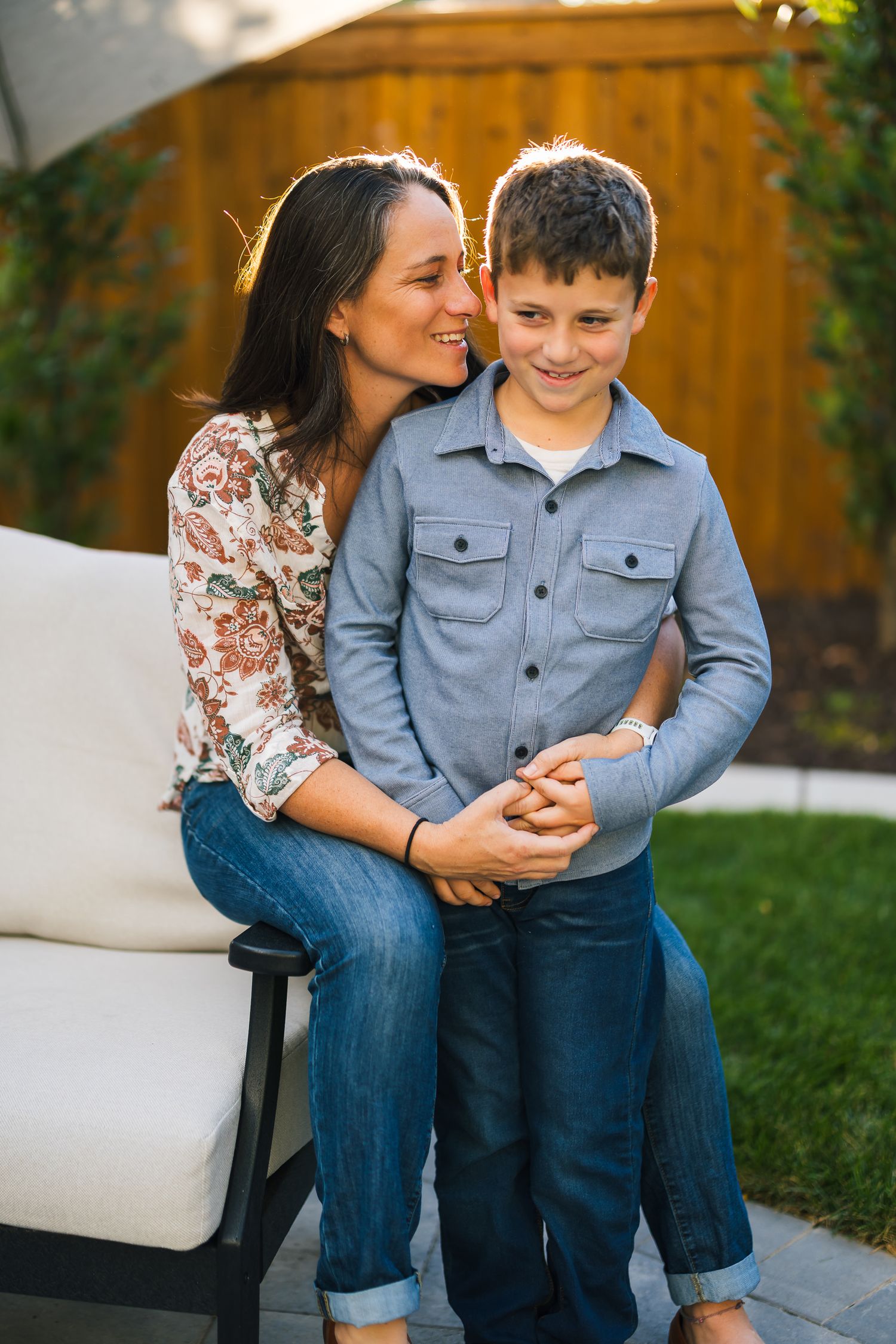 A sweet moment shared between parent and child sitting together on an outdoor patio couch against a wooden fence.