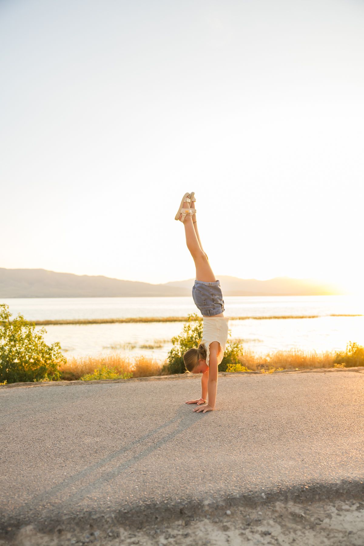 Person performing handstand silhouetted against sunset sky over water.