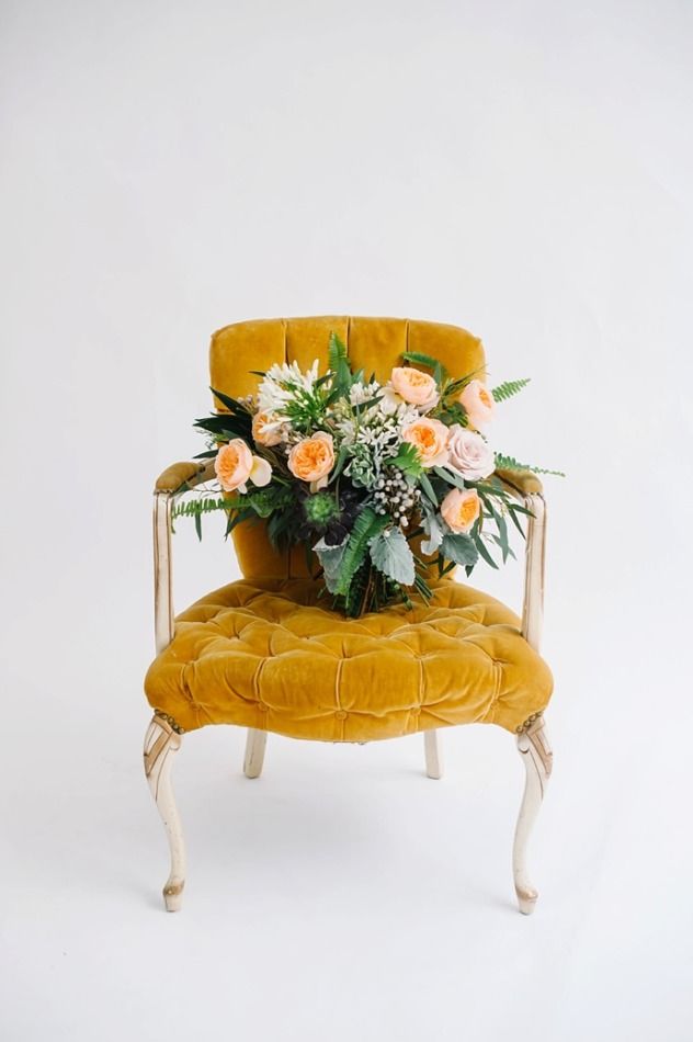 Elegant mustard yellow velvet chair adorned with pink and peach floral arrangement.